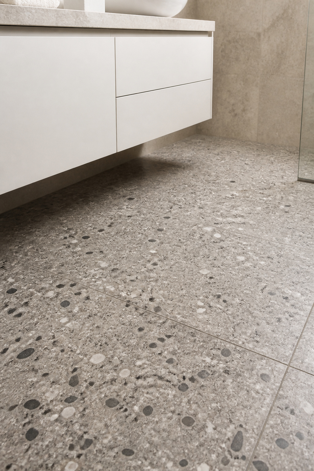 Warm grey terrazzo with cream and charcoal chips — used on the floor only, so it reads as the room's one expressive element rather than competing with itself on every surface.