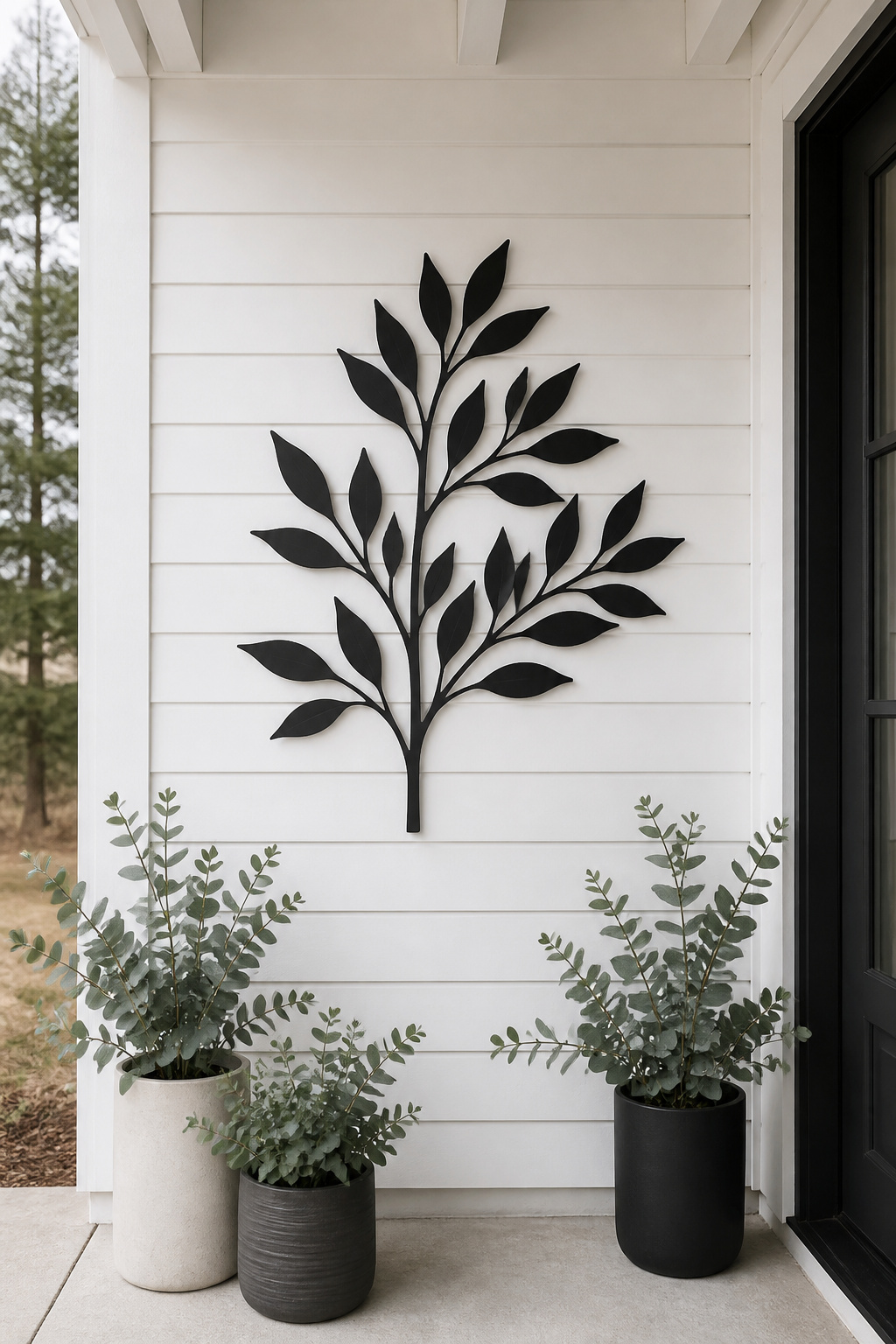 One large botanical silhouette in powder-coated matte black against white siding — the Scandinavian principle of one strong piece over many small ones, applied to porch wall art.