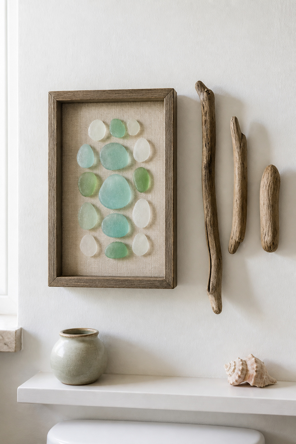 A shadow box of sea glass and a driftwood arrangement bring the narrative of things gathered over time — the authenticity that mass-produced coastal prints cannot offer.