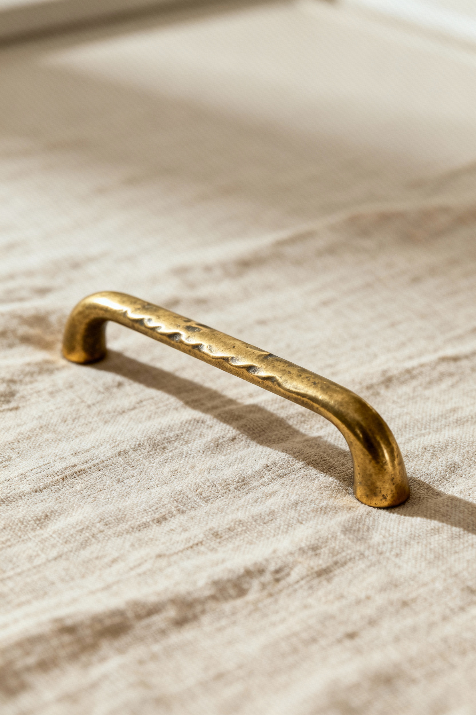 Close-up of an ethically sourced, artisanally crafted brass kitchen cabinet pull showcasing its unique textures on a linen background, emphasizing quality and origin.