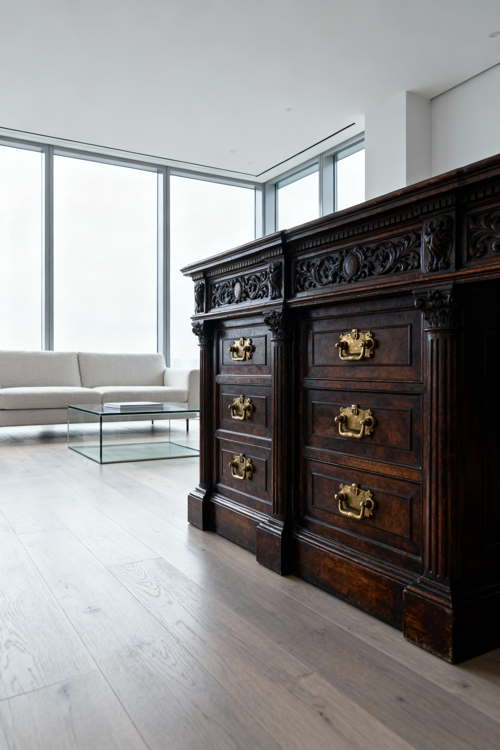 A brooding, dark mahogany antique Victorian partner’s desk anchors a bright, high-ceilinged minimalist living room with white walls and expansive glass windows, demonstrating the grounding effect of traditional brown furniture in contemporary design.
