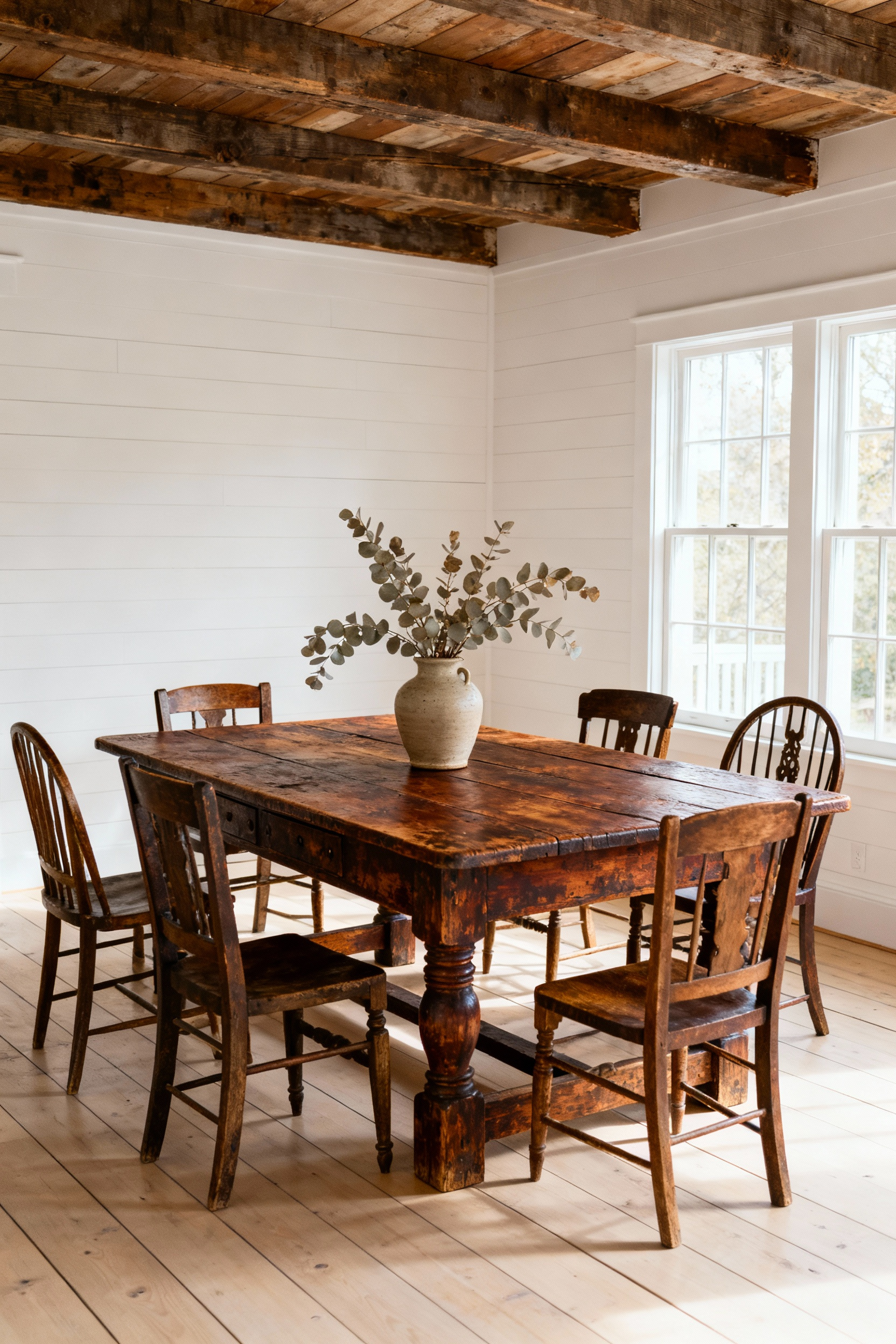 Rustic farmhouse dining room showcasing an antique wooden heirloom table with vintage chairs and natural light.