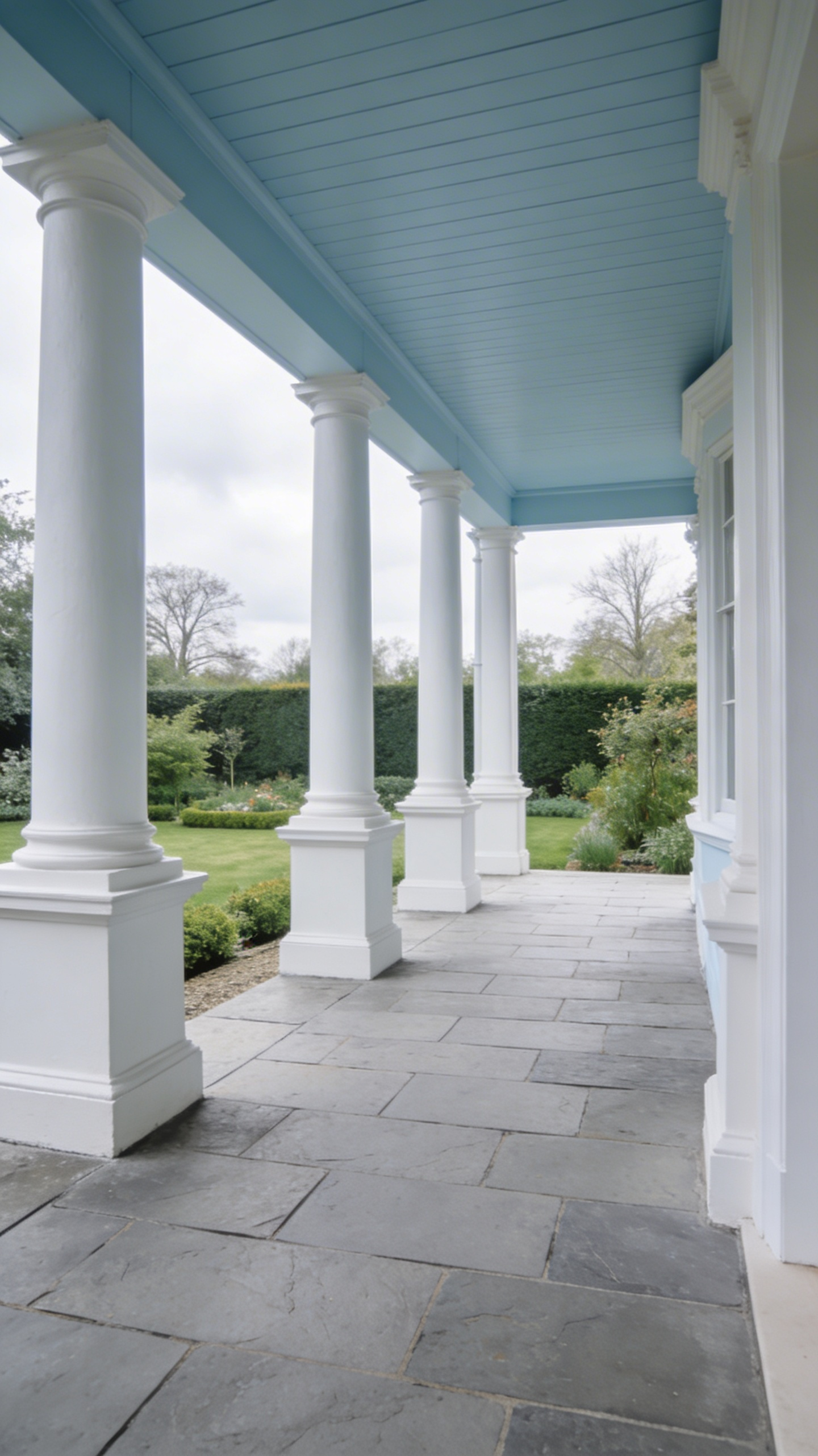 A wide-angle view of a traditional British porch featuring a subtle haint blue ceiling and white pillars set against a soft grey sky.