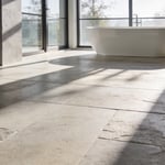 A modern luxury bathroom featuring large brushed limestone floor tiles and a minimalist freestanding tub bathed in natural light.