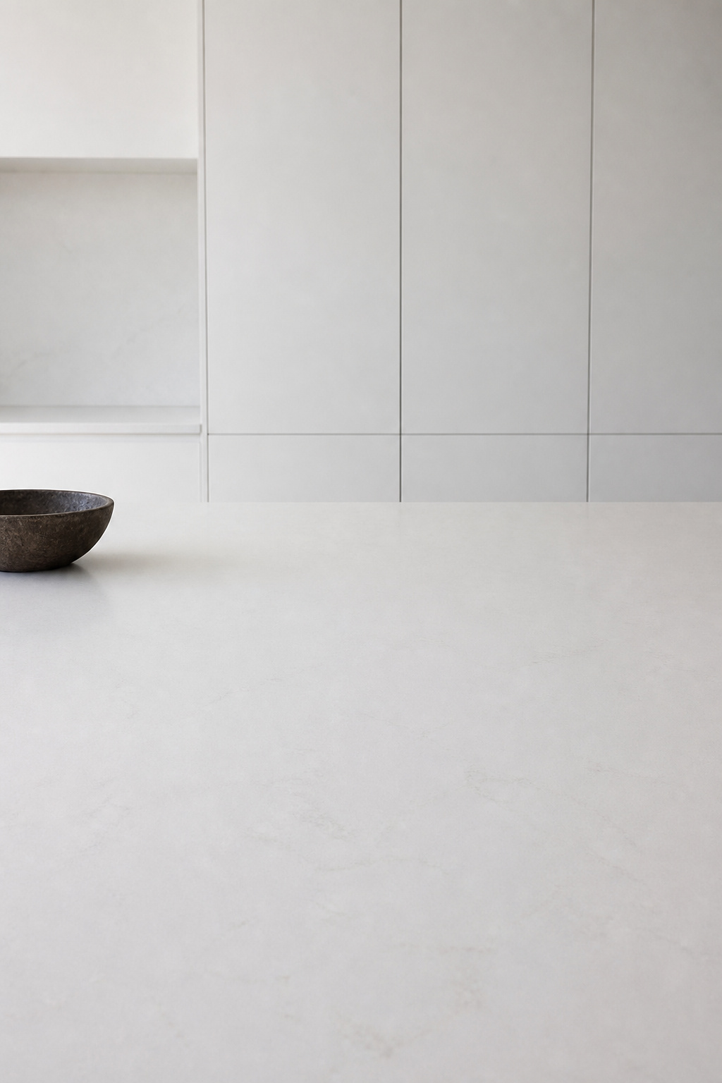 A kitchen where the most prominent element is what isn't there — the bare worktop occupying most of the frame, a single ceramic bowl the only object in the room.