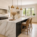 A complete view of a sophisticated black kitchen island kitchen — brass hardware, marble waterfall counter, brass pendants, and the confidence of deliberate contrast.