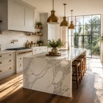 A beautifully proportioned kitchen with pale dove gray Shaker cabinets, Calacatta marble waterfall island, and brushed brass hardware — the quintessential sophisticated gray kitchen.