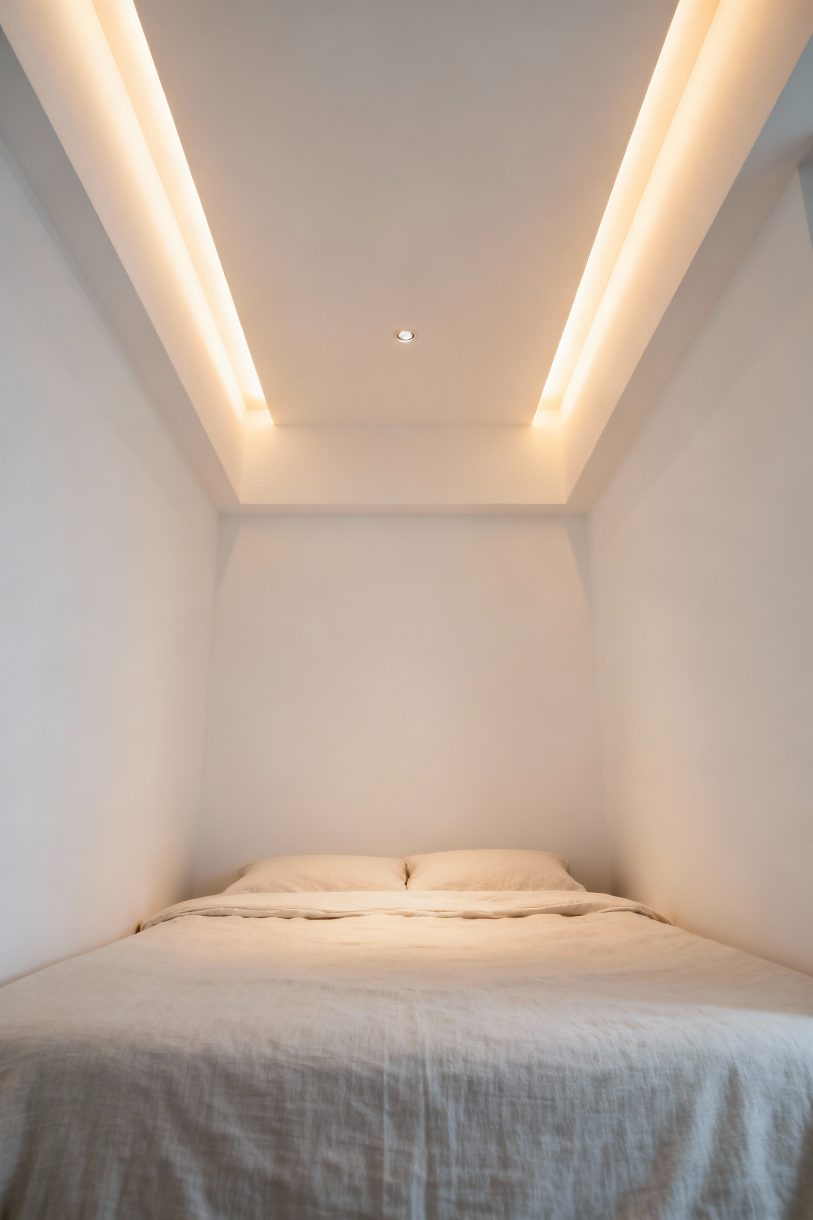 Minimalist small bedroom with a bed and recessed lighting fixtures integrated into the ceiling, enhancing headroom and spatial perception.