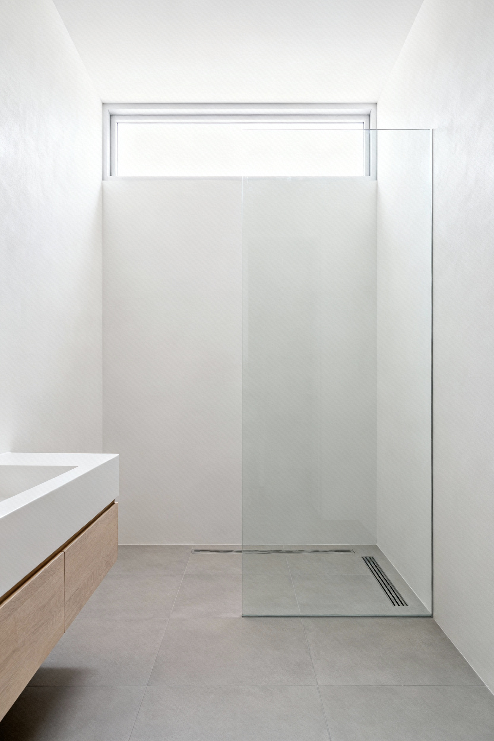 Seamless curbless wet room design in a small bathroom, featuring uninterrupted large-format light gray floor tiles to visually expand the space.