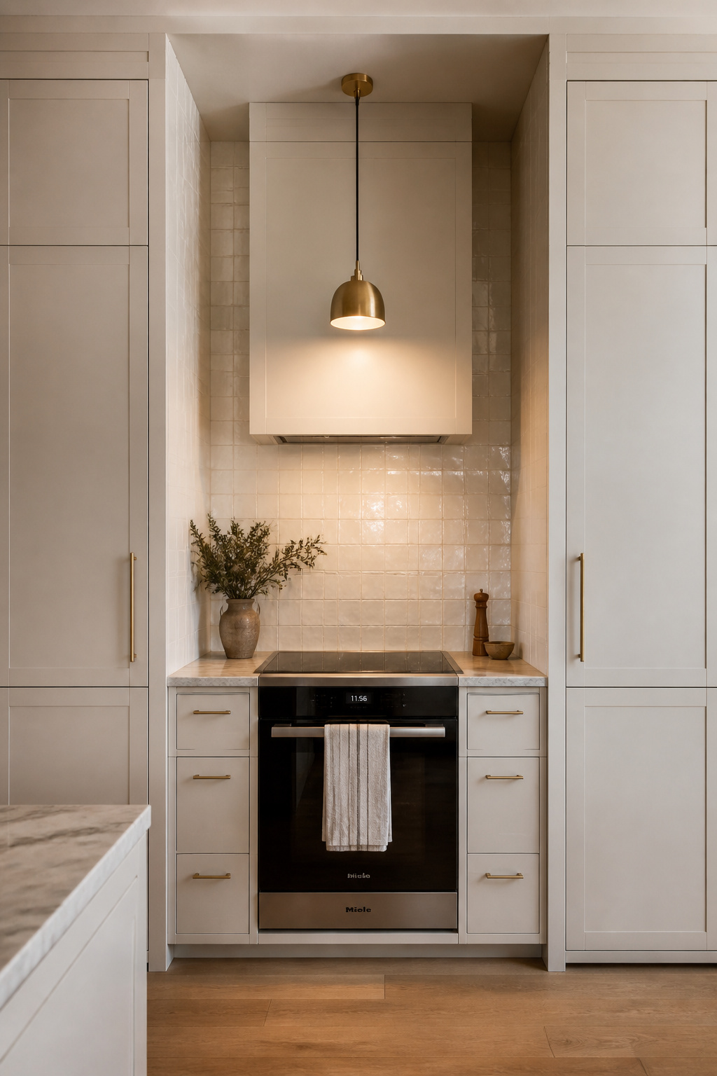 Two full-height cabinetry columns frame a cooking alcove with a concealed hood and zellige-tiled interior — the most architecturally resolved way to define the cooking zone.