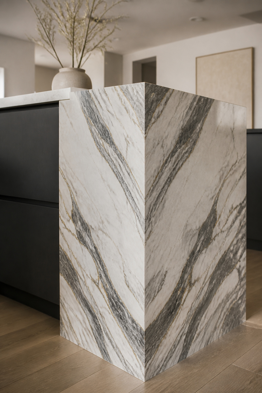 A book-matched marble waterfall cascades from island countertop to floor in a single continuous slab, treating the island as a sculptural object rather than a cabinet with a top.