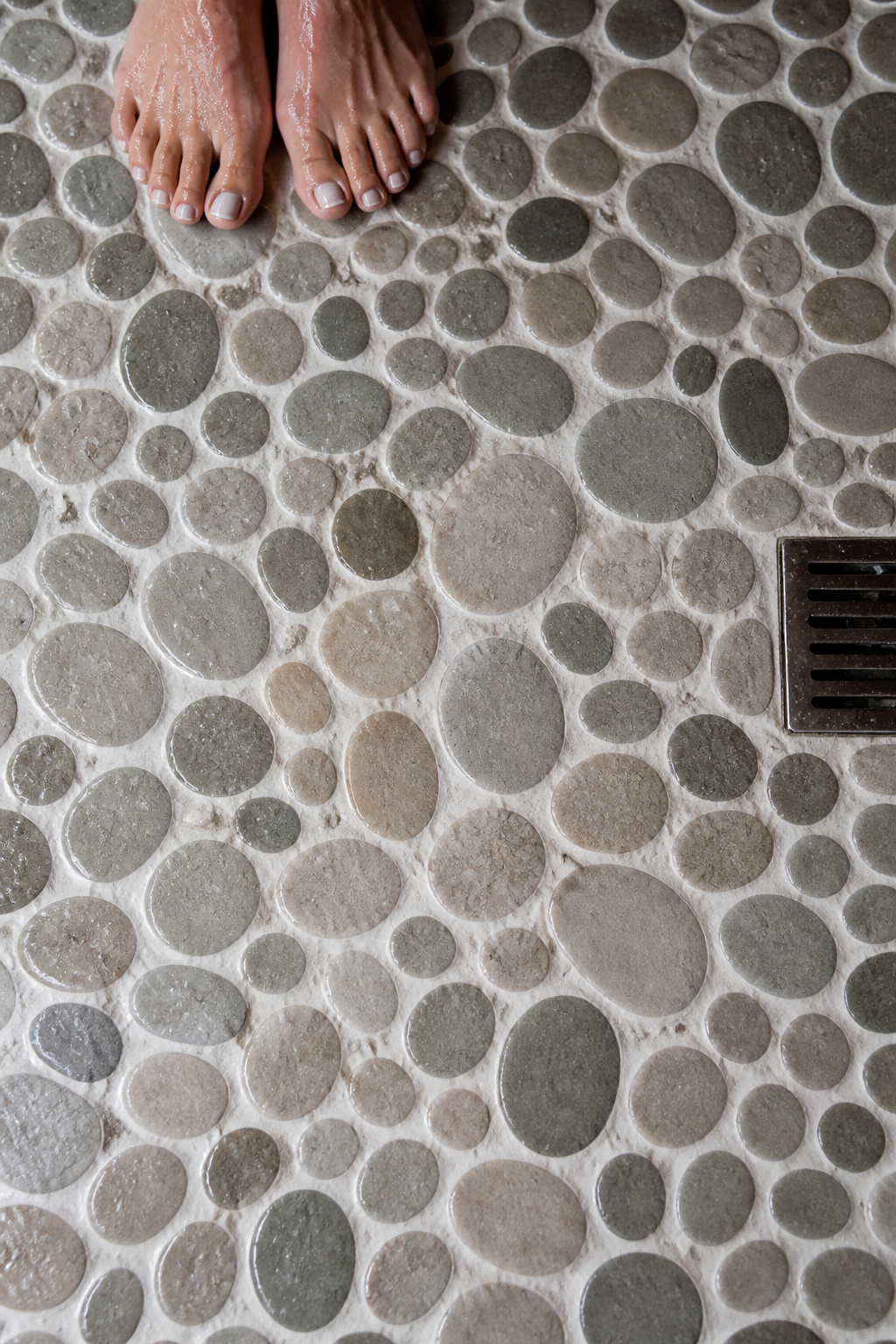 Natural river pebble shower floors bring tactile biophilic warmth to a coastal bathroom that no flat tile can replicate.