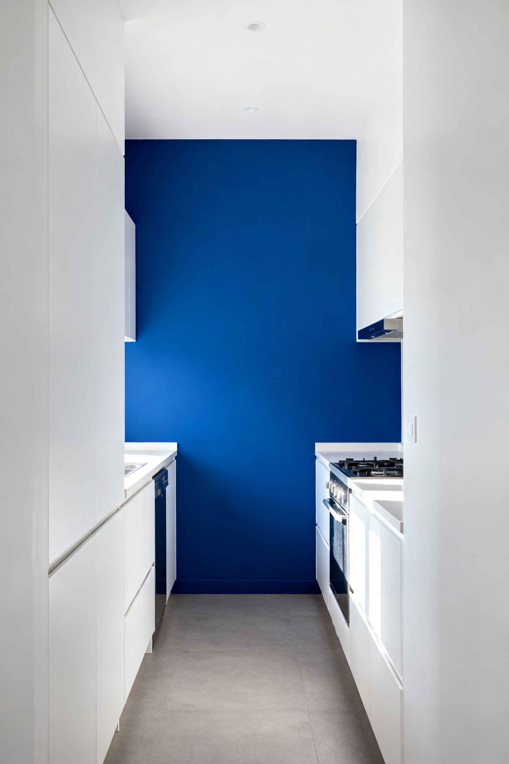 A modern galley kitchen interior featuring intentional color blocking, with a vibrant sapphire blue accent wall contrasting with white cabinetry, to sculpt perceived spatial depth.
