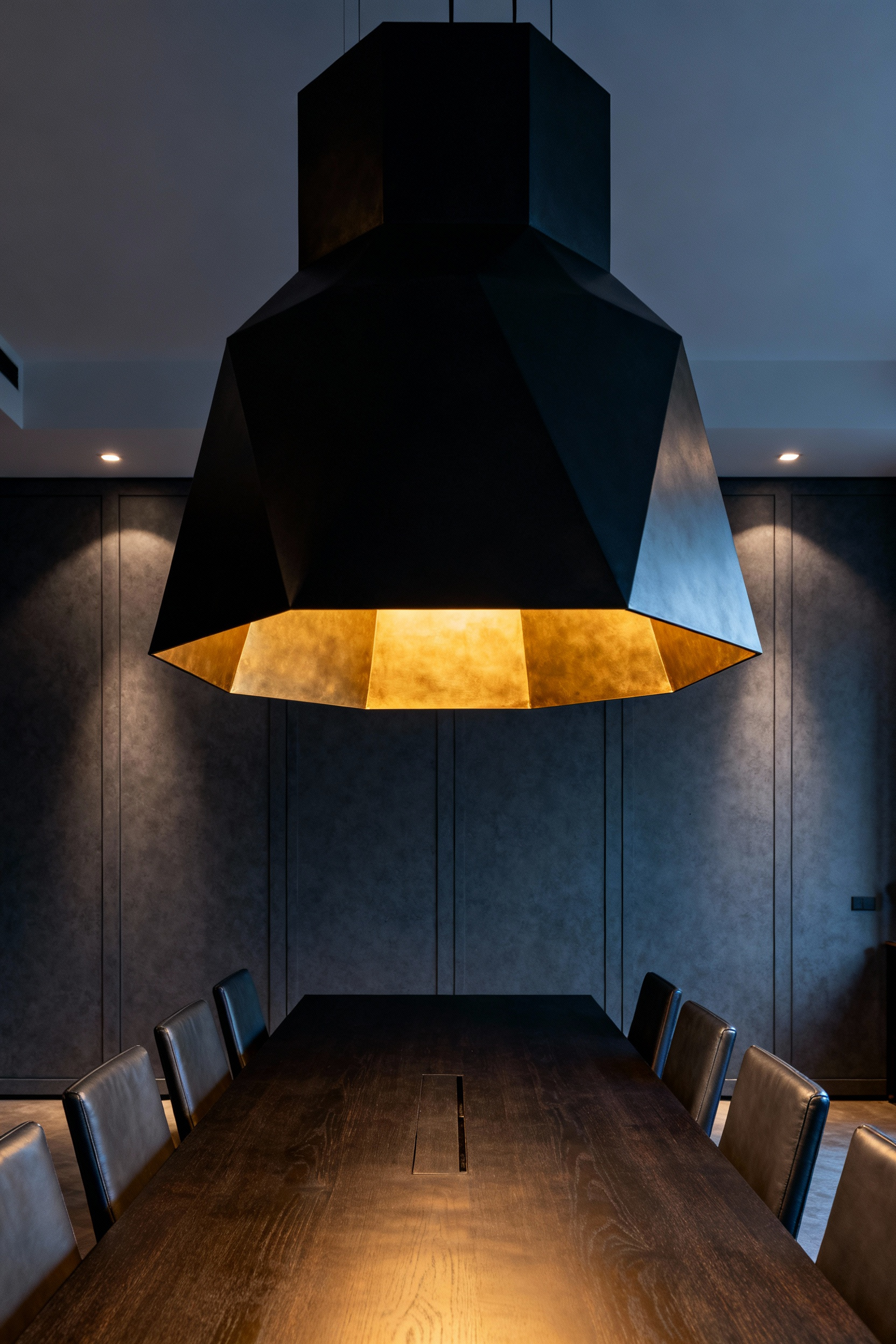 Oversized, dramatic sculptural light fixture made of black metal and brass dominating a long dark walnut dining table in a contemporary charcoal gray dining room. The fixture demonstrates the modern trend of bold proportions.