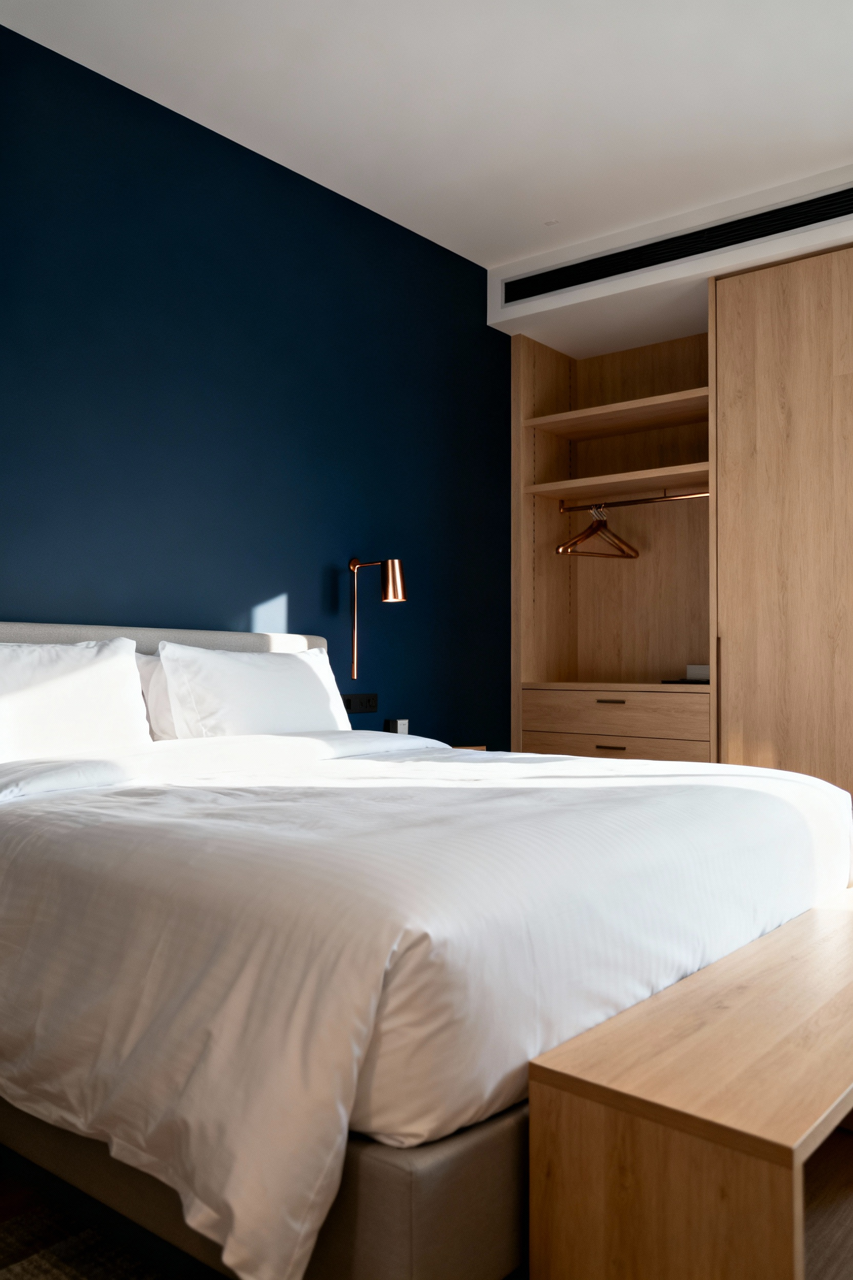A serene bedroom featuring a deep navy blue feature wall behind a bed with crisp white bedding and light wood furniture, enhancing architectural depth and a tranquil atmosphere.