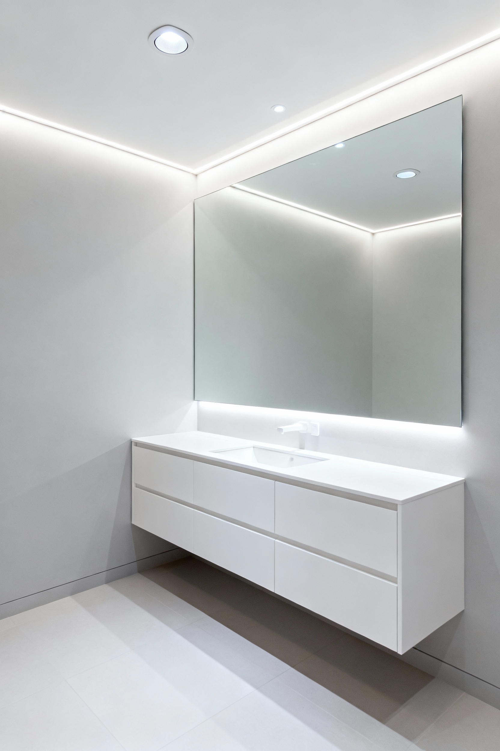 Small bathroom featuring bright light-colored walls, a floating white vanity, a large frameless mirror, and integrated LED lighting, giving an illusion of a larger, well-lit space.