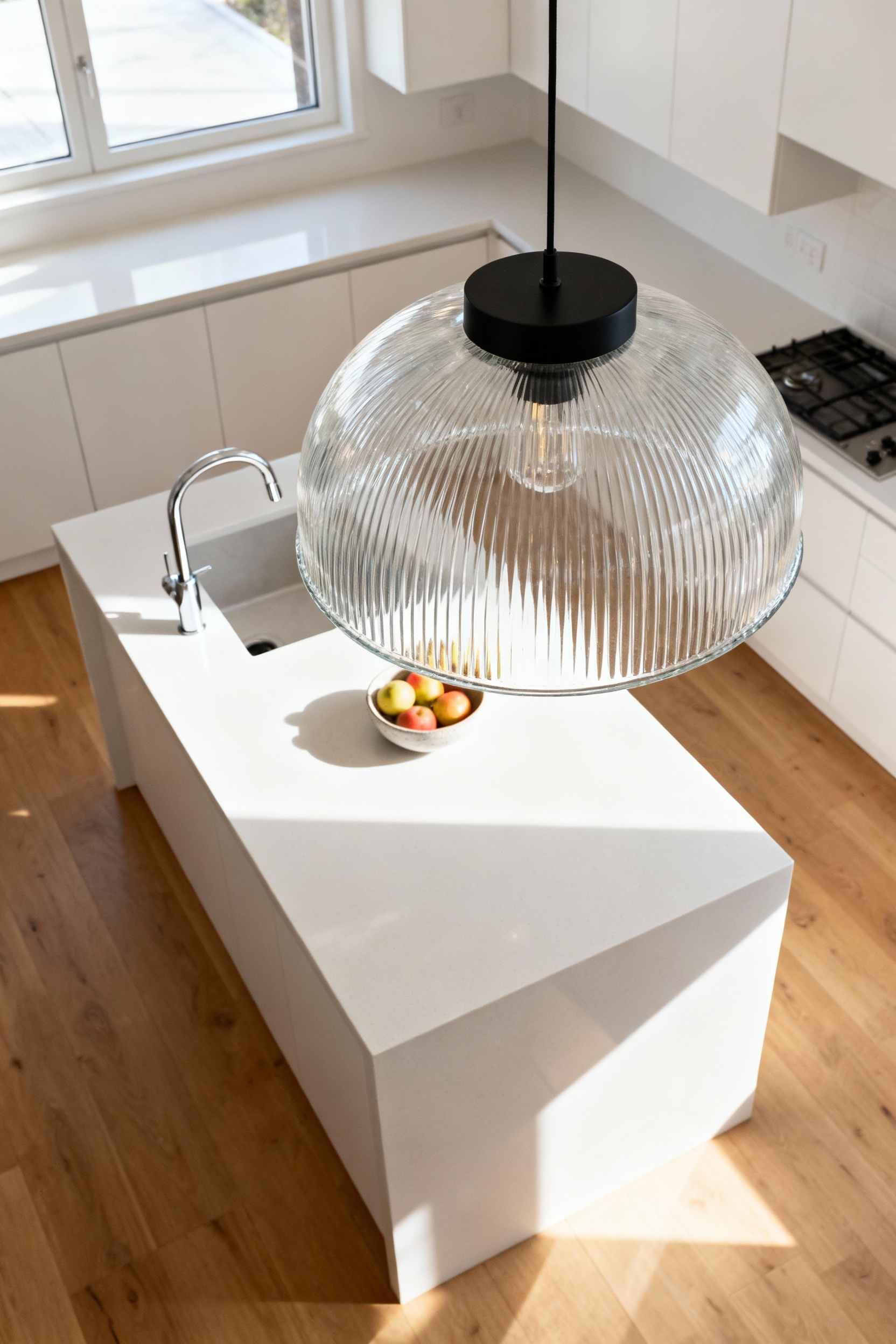 Small kitchen decor ideas featuring a singular, oversized clear glass pendant light fixture anchoring a minimalist white quartz island and sleek white cabinetry.