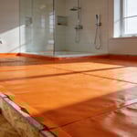 A comprehensive view of a bathroom renovation project showing the installation of a modern orange waterproofing membrane over the floor foundation.