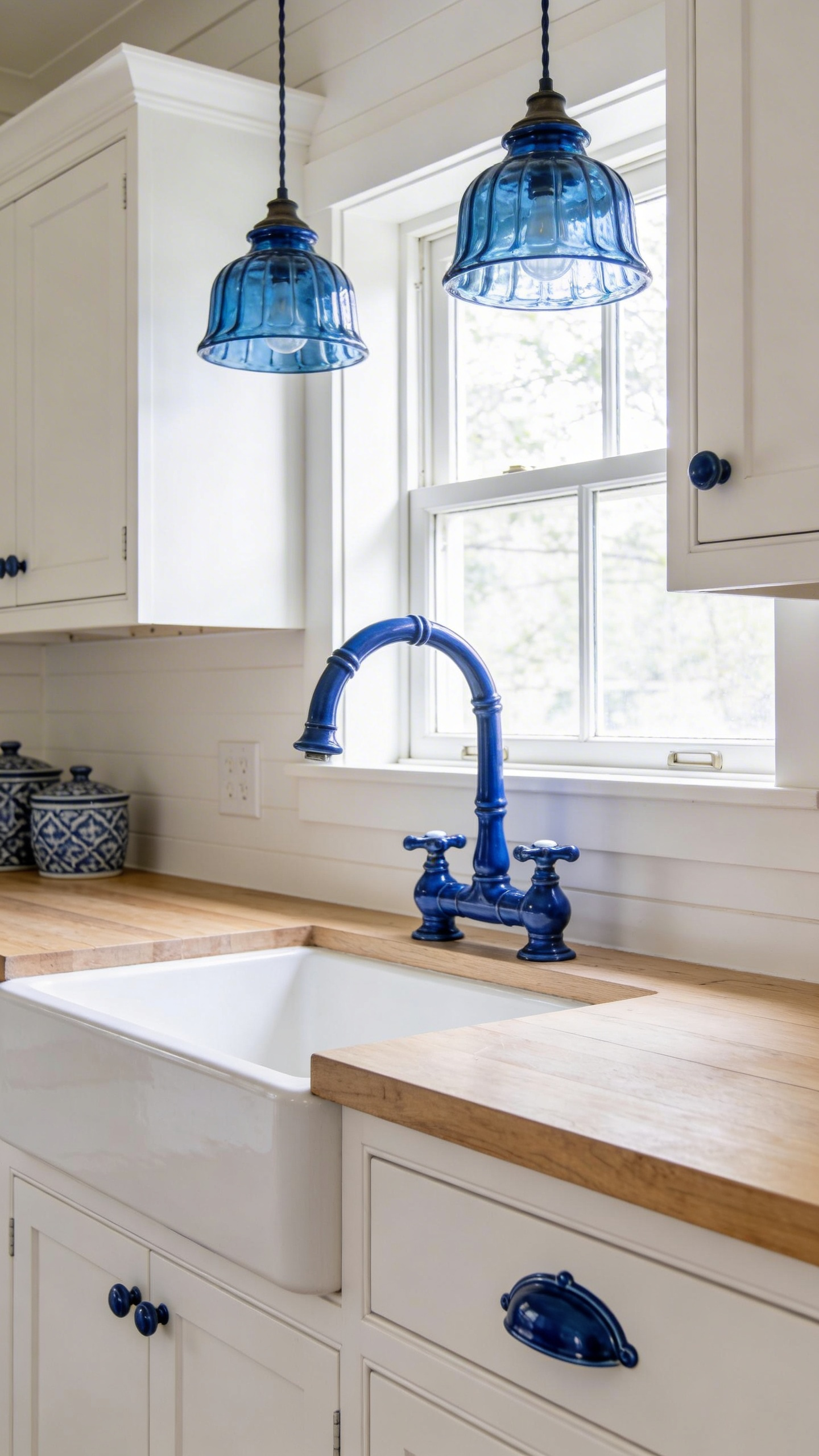 Blue ceramic hardware and blue glass pendants on neutral white cabinetry — the jewellery approach to introducing blue kitchen colour with zero structural commitment.