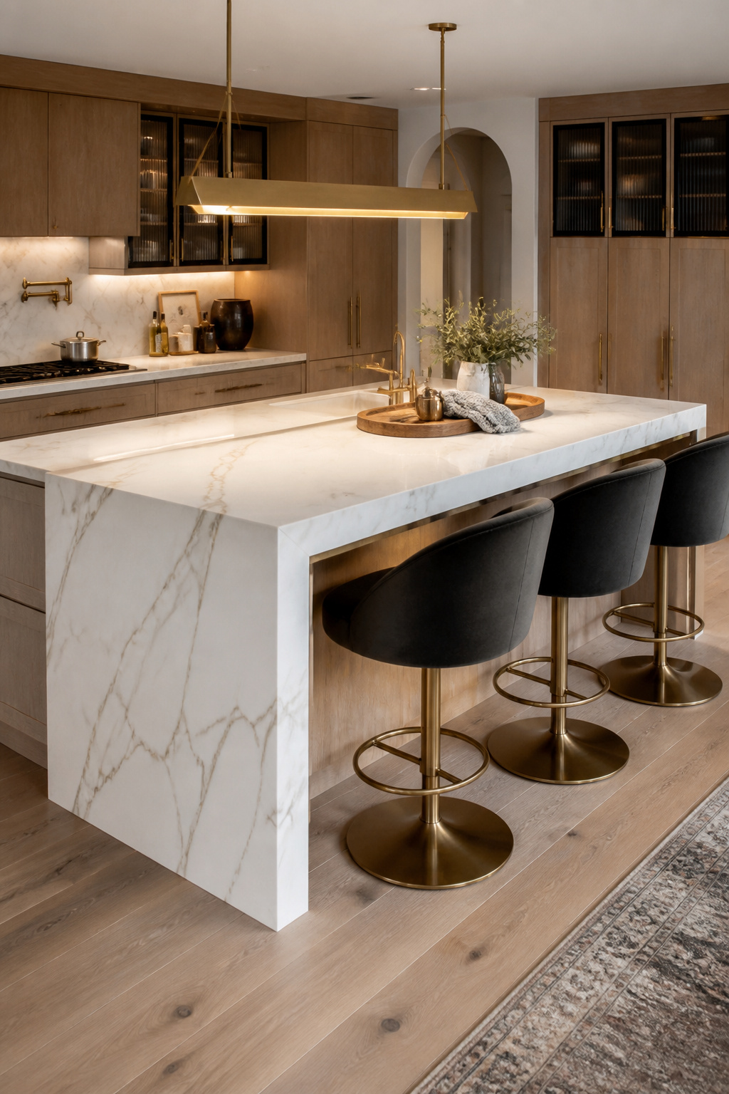 A raised Calacatta quartz waterfall island with charcoal velvet swivel stools makes the kitchen bar seating zone as beautiful from across the room as it is functional at close range.