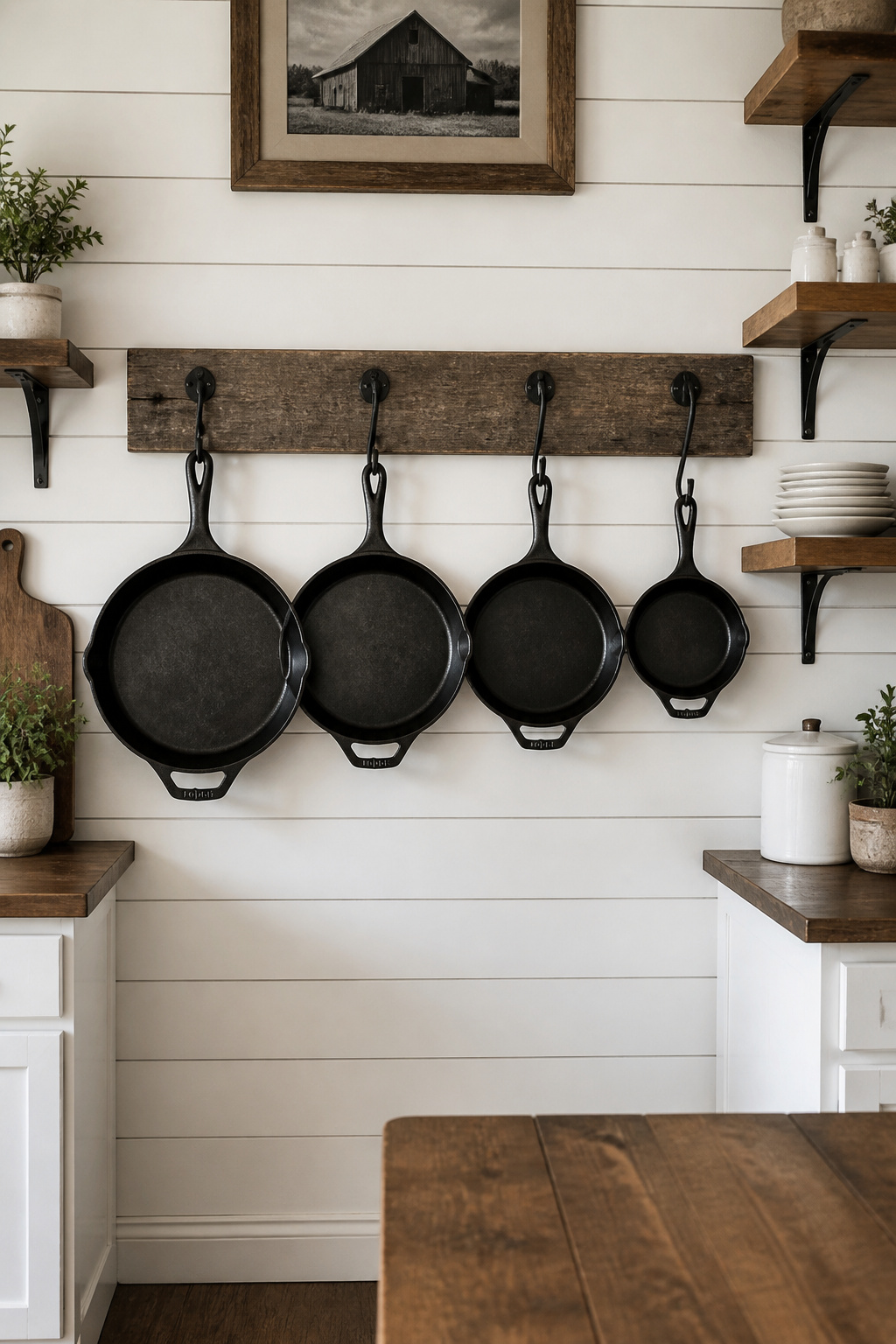 A row of cast iron skillets hung from a barn wood rail — the most functional piece of farmhouse kitchen wall decor, and the easiest to justify.