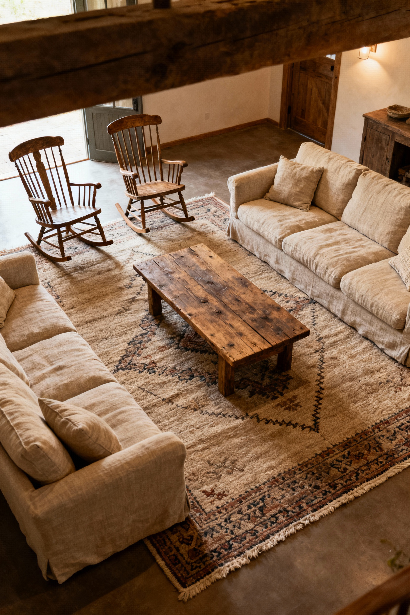 A beautifully arranged country living room featuring a U-shaped linen sectional, rocking chairs, and a reclaimed wood coffee table on a wool rug, designed for comfort and conversation.