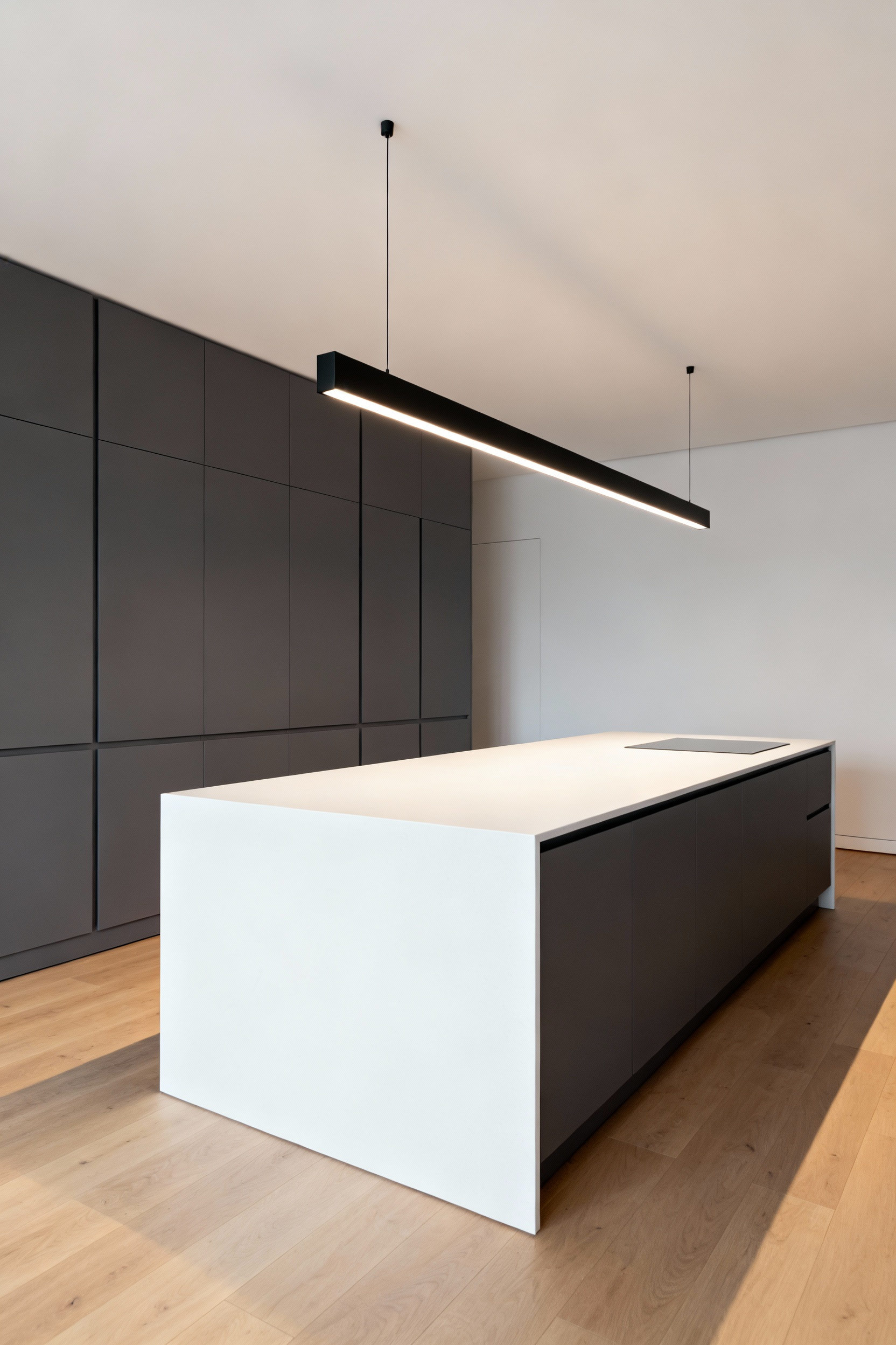 A modern kitchen featuring a sleek, matte black linear suspension light fixture providing uniform, glare-free illumination over a white quartz island.