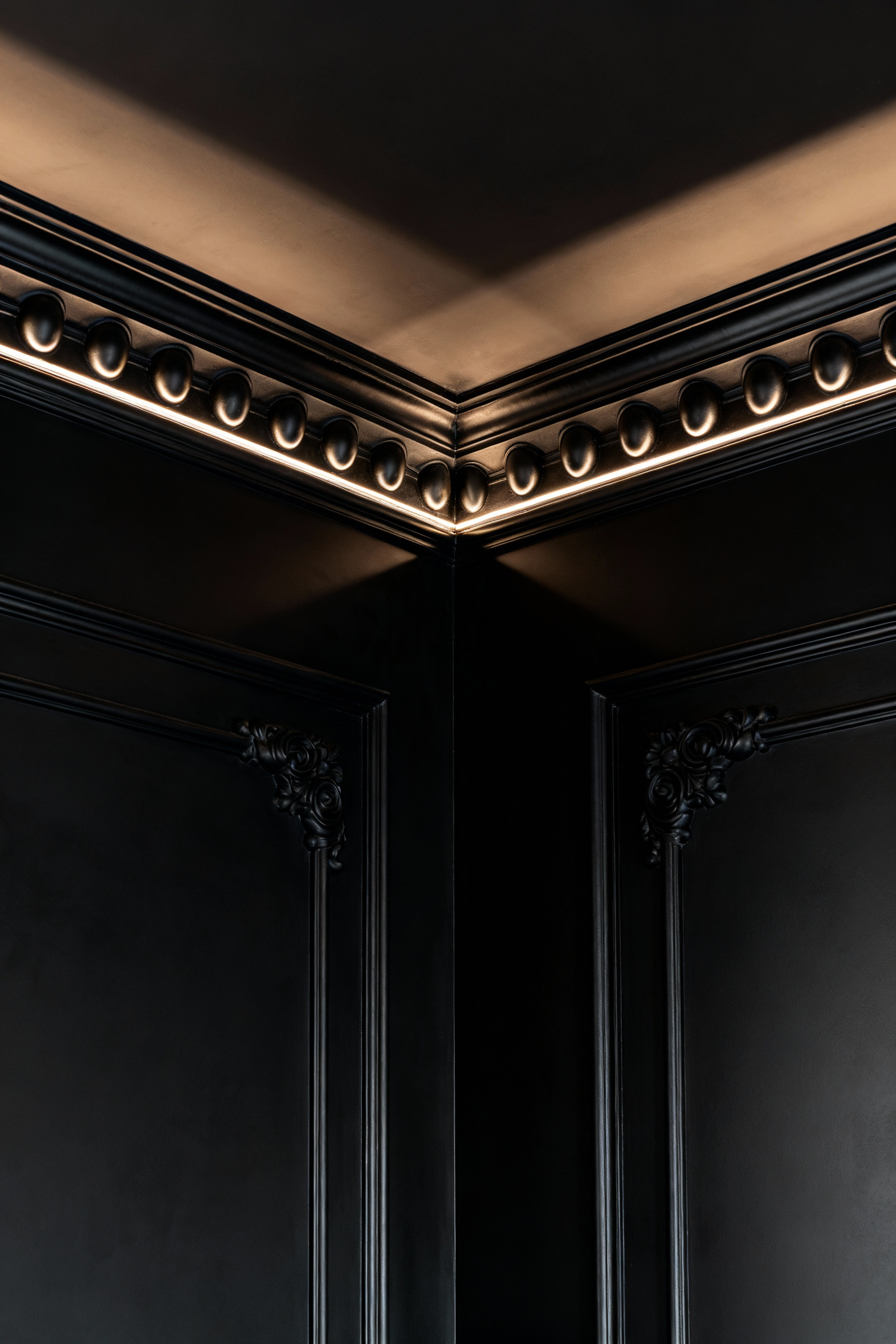 Intricate black moldings and cornices in a sophisticated black dining room, artfully detailed with dramatic shadows and varying black sheens to create sculptural depth.