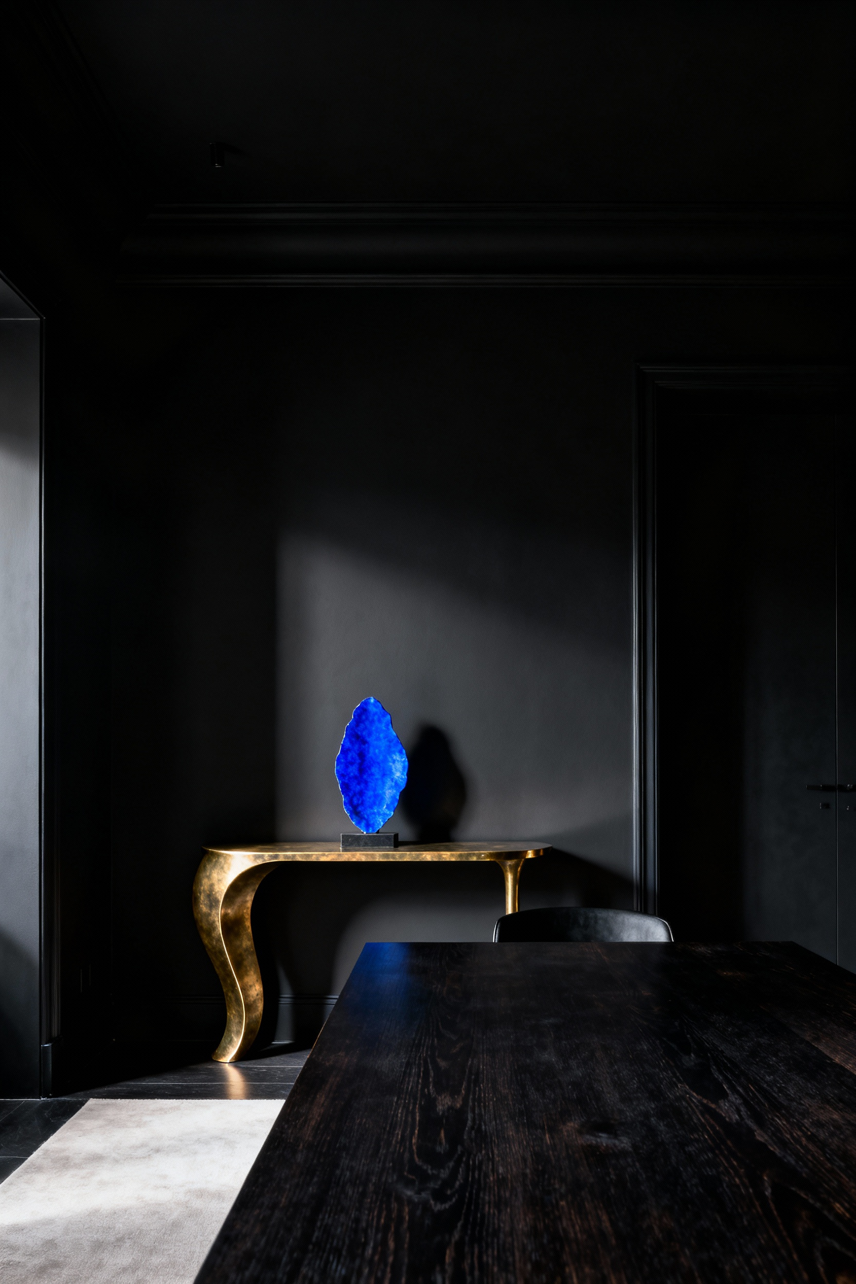 Luxurious black dining room featuring a patinated brass console table and sapphire blue abstract art, creating a calibrated pop of color.