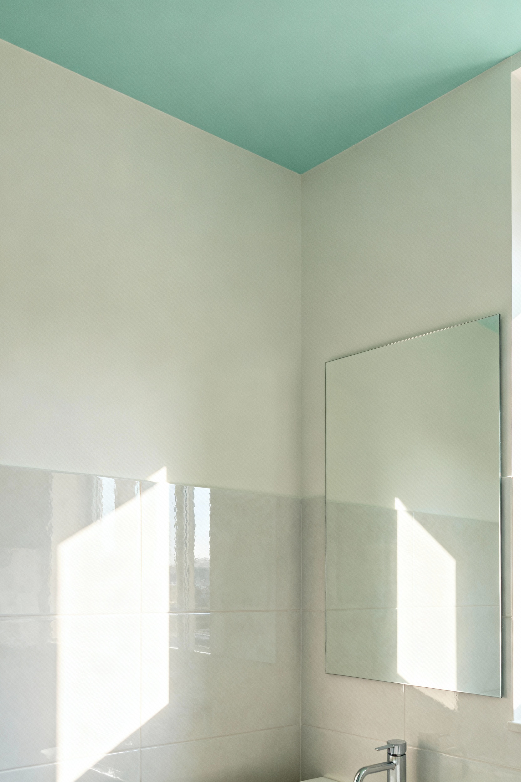 Small bathroom with light-reflecting off-white and muted aqua walls, large frameless mirror, and polished tiles, showcasing an expansive and serene color palette.