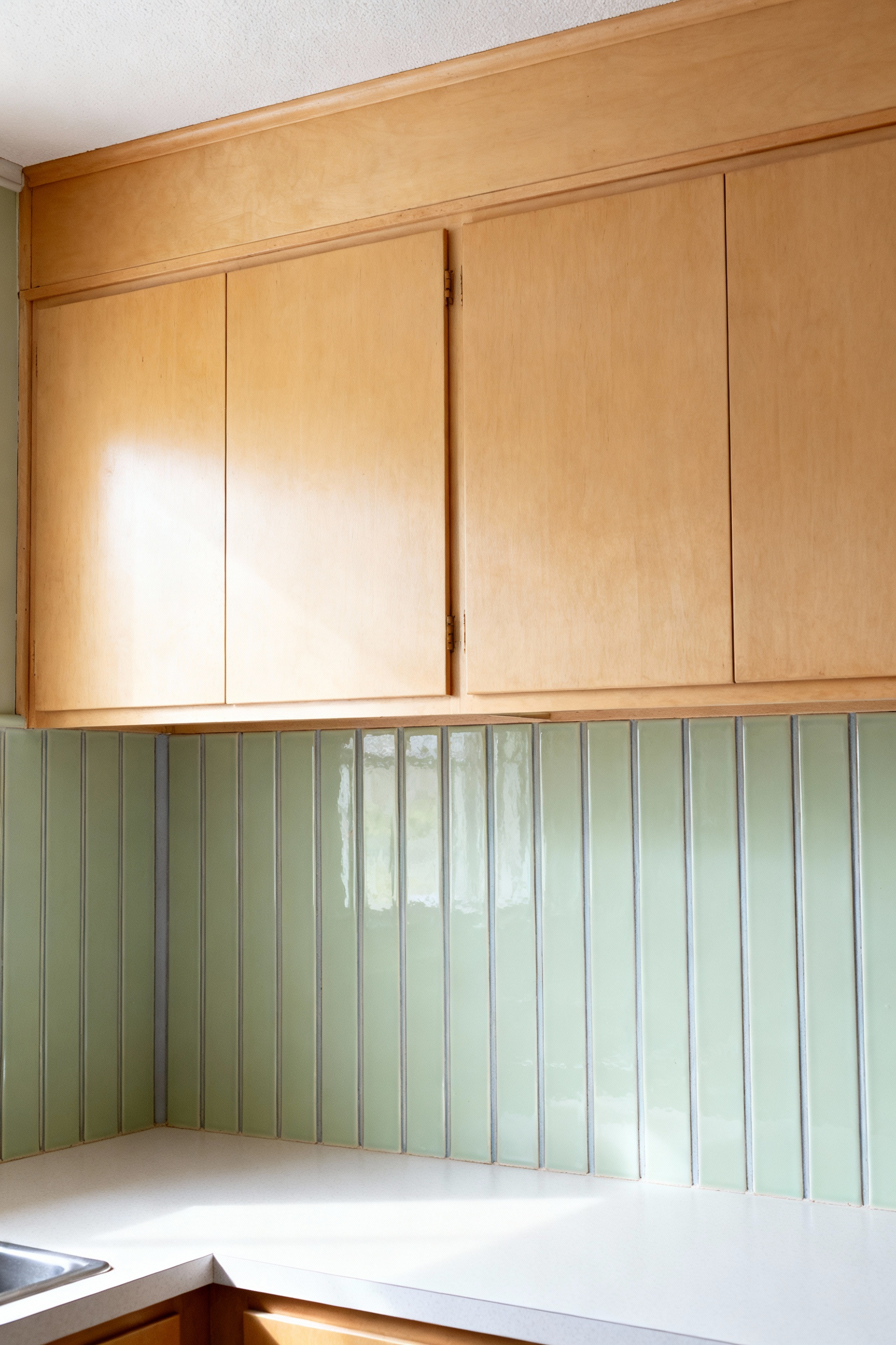 A mid-century galley kitchen showcasing a straight vertical stack backsplash pattern using sage green rectangular tiles, a design technique used to visually heighten the low ceilings typical of 1950s ranch homes.
