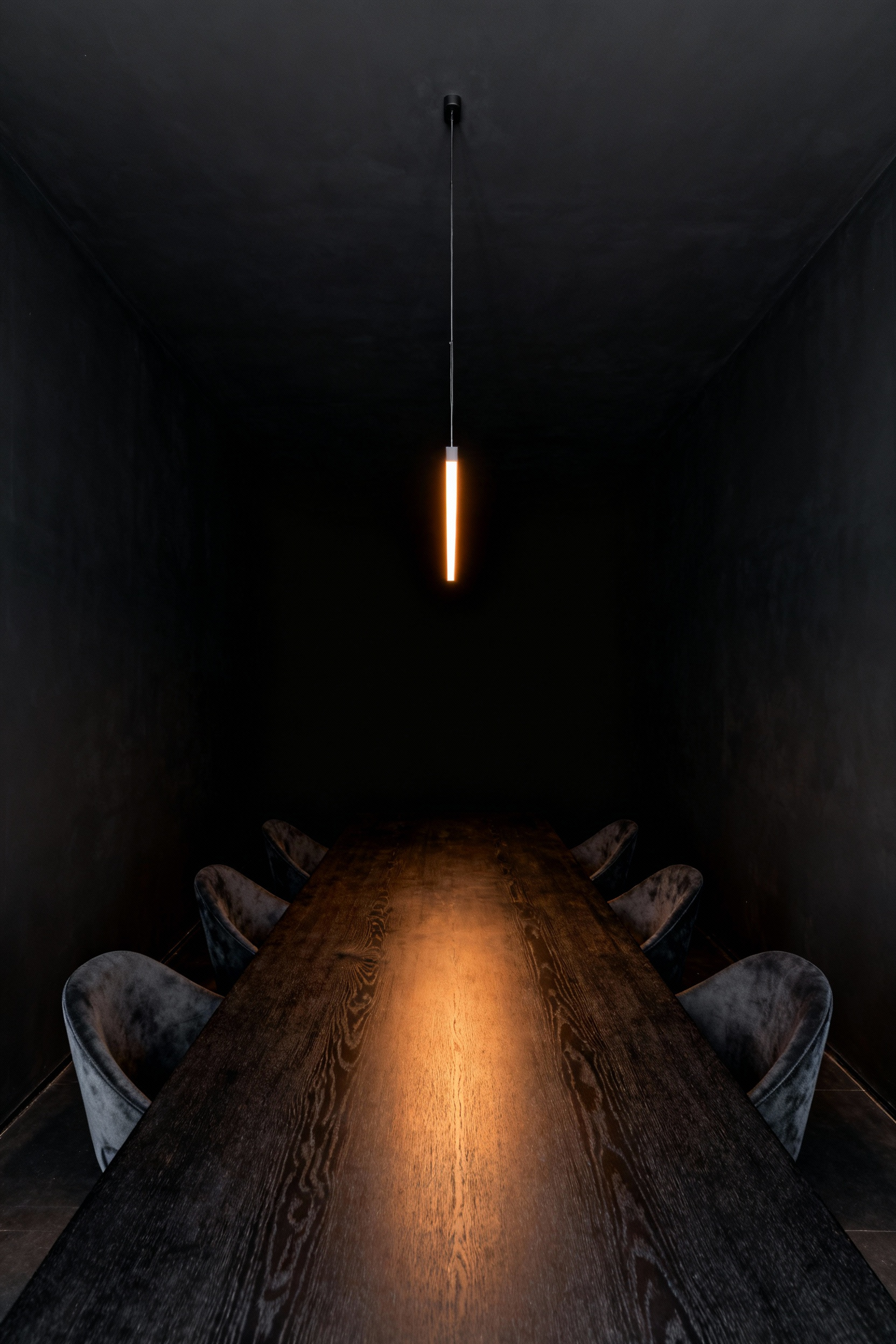 A hyperrealistic photo of a minimalist dining room with matte black walls and ceiling that absorb light, giving the illusion of limitless depth and a dramatic, cocoon-like void, lit only by a warm pendant over the dark wood table.