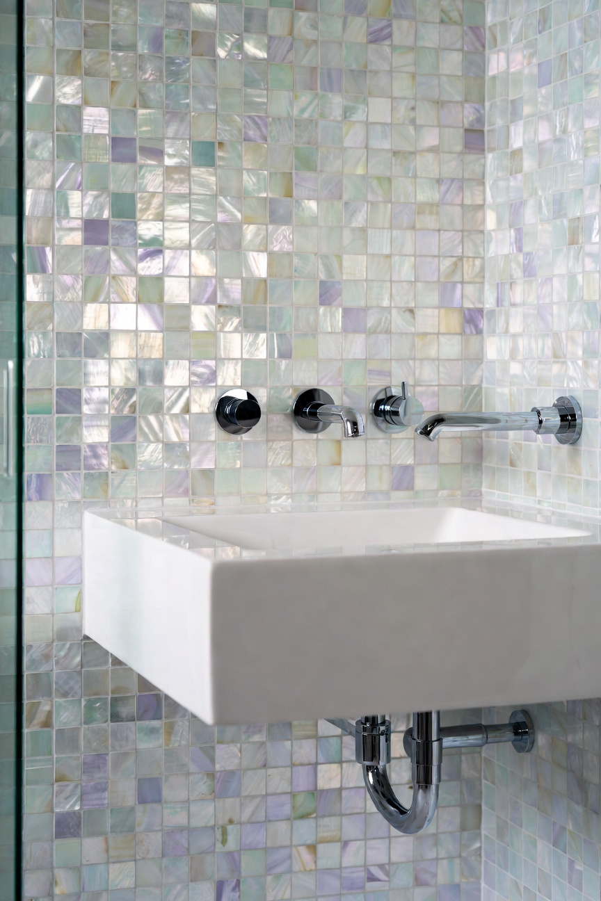 A luxurious coastal bathroom featuring a Mother of Pearl mosaic tile accent wall that shimmers with ethereal pastel iridescence under soft morning light.