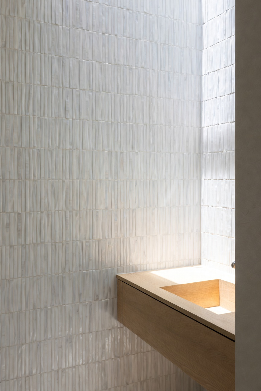 Modern coastal bathroom wall covered in vertically stacked, pale cream Kit-Kat finger mosaic tiles, designed to resemble dune grass texture, above a light oak floating vanity.
