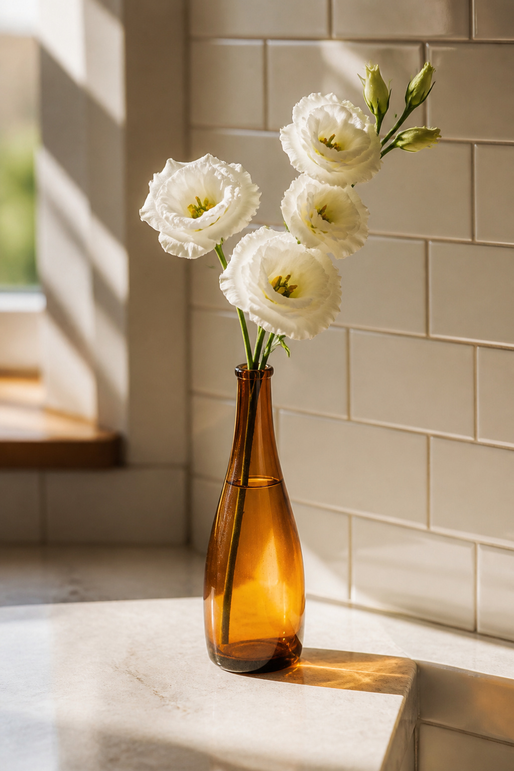 A single white lisianthus stem in a narrow amber glass bud vase on a light stone kitchen counter, morning light catching the amber glass.