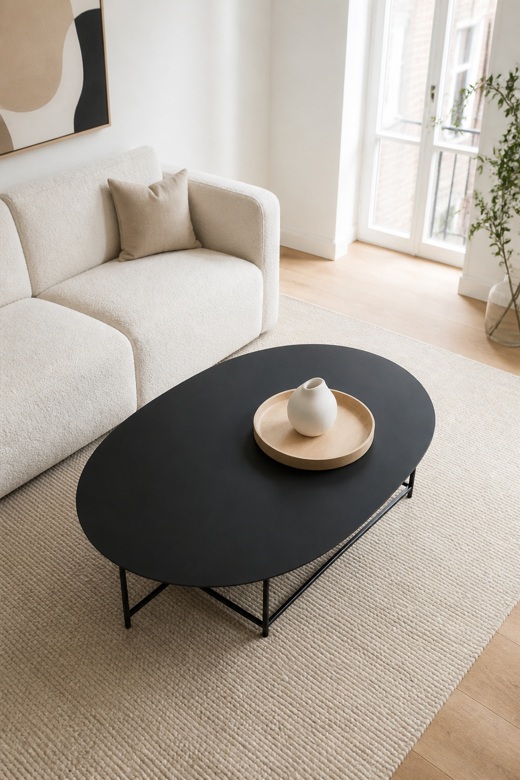 A matte black oval coffee table creates a strong visual anchor in a light-filled Scandinavian living room, proving that dark and pale can coexist beautifully.