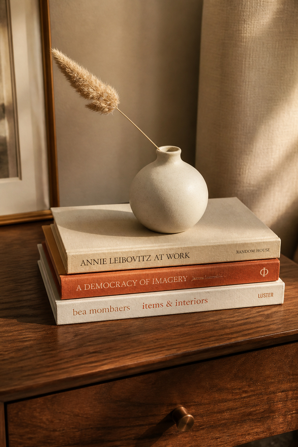 A stack of neutral hardbacks grounds this end table vignette, with a small ceramic vase on top doubling as both sculpture and botanical holder.
