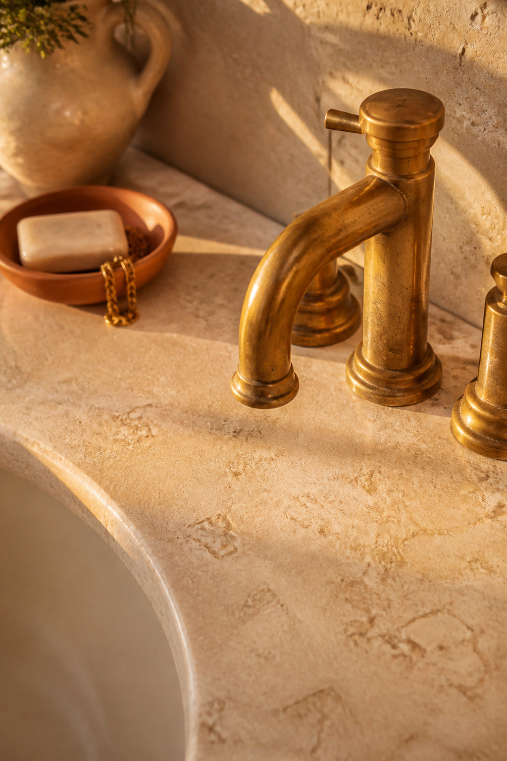 A warm ivory travertine countertop, filled and honed, paired with an unlacquered brass faucet showing early patina.