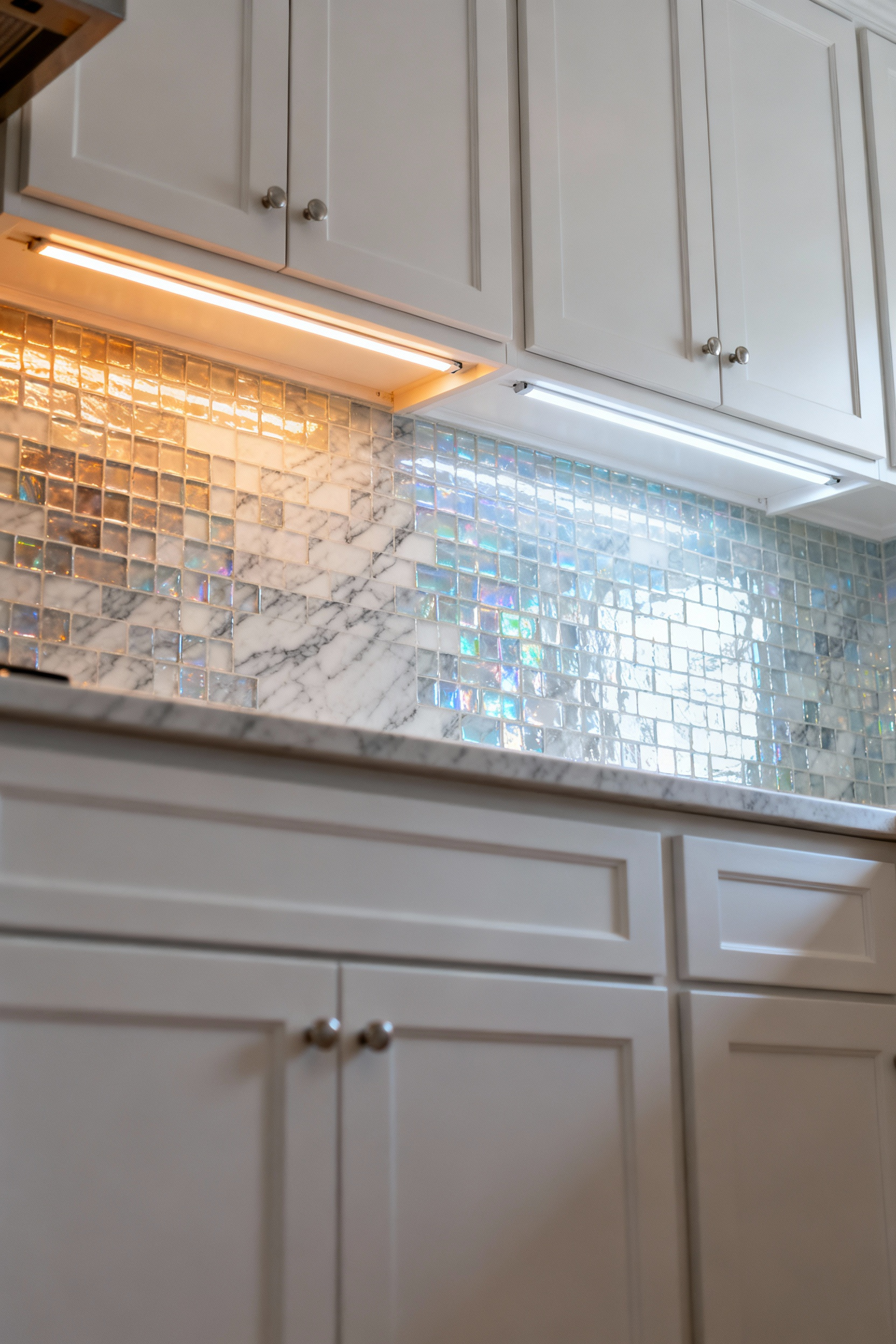A modern white kitchen backsplash, half illuminated by warm under-cabinet lighting, and the other half by cool under-cabinet lighting, showing distinct changes in perceived marble tone and veining texture.