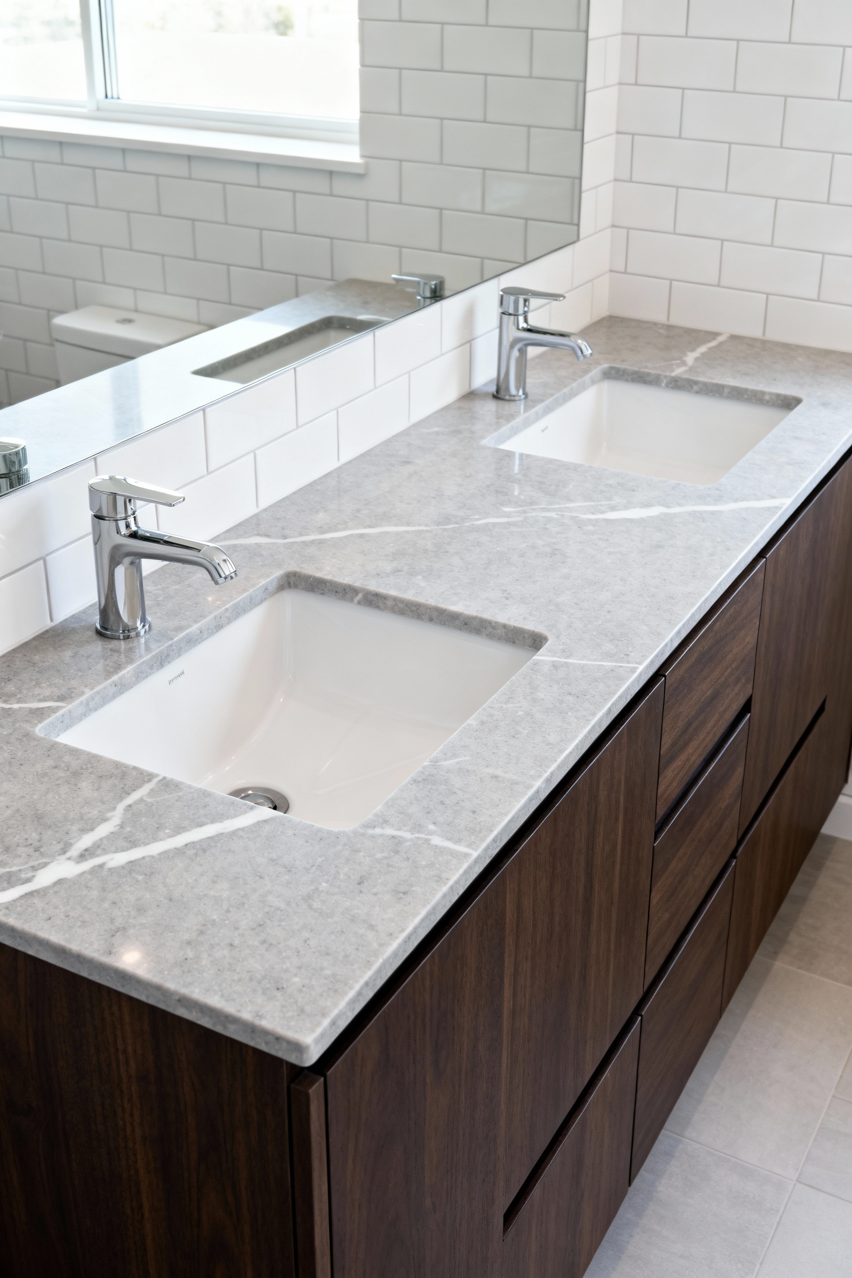 A sleek double vanity countertop made of highly polished light grey engineered quartz in a modern, naturally lit bathroom.