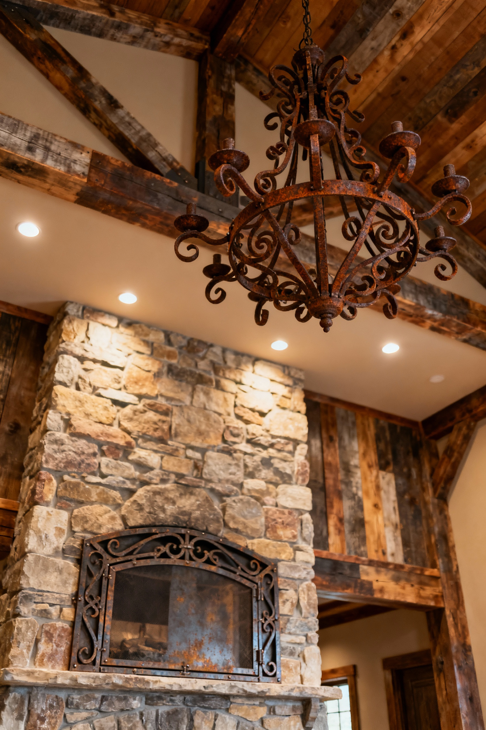 A rustic living room featuring a grand hand-forged wrought iron chandelier with a deep oxidized patina and an artisan-crafted fireplace screen, showcasing natural metal textures.