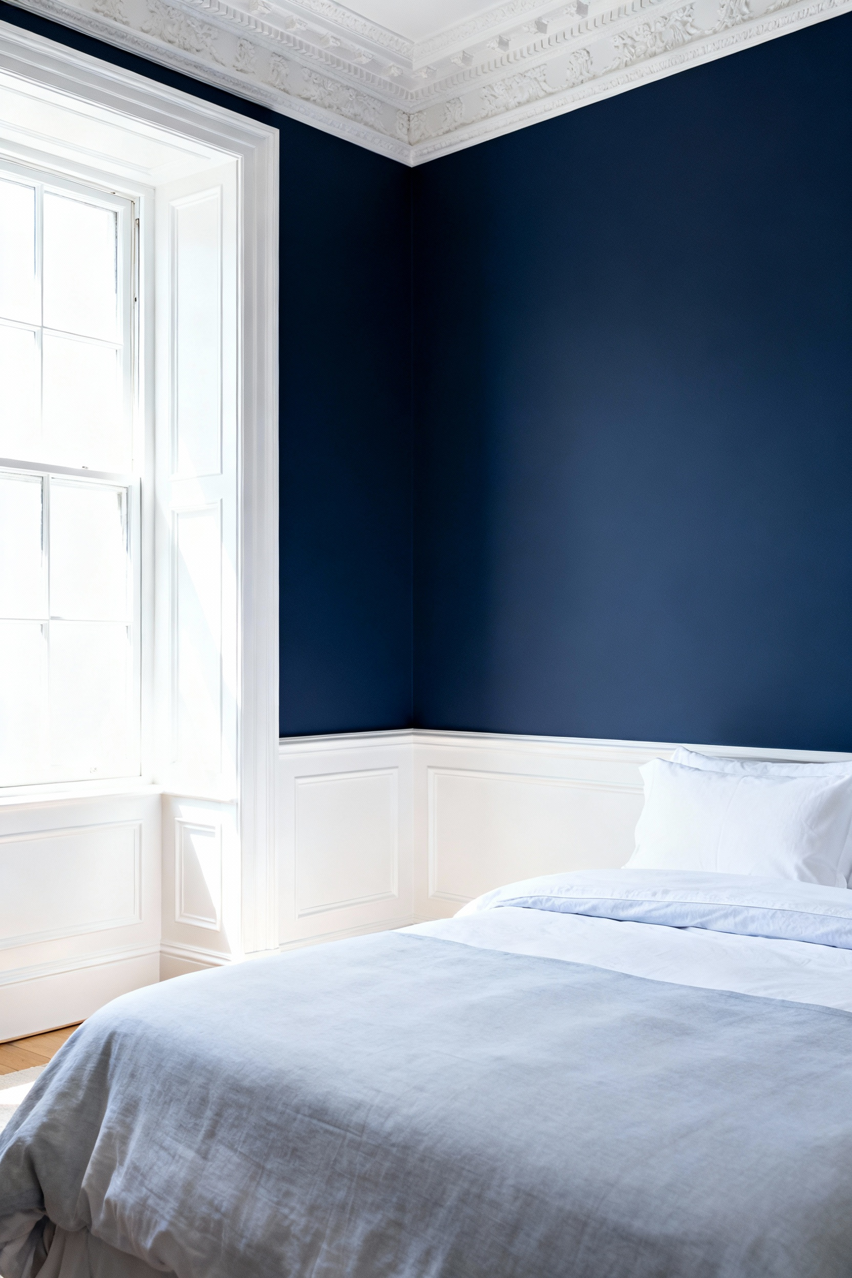 A sophisticated bedroom featuring deep royal blue walls offset by crisp, pure white semi-gloss crown molding, wainscoting, and baseboards, illustrating a high-contrast architectural definition.