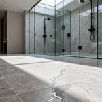 Seamless luxury bathroom flooring made of high-density porcelain tiles replicating the organic grain of honed taupe limestone in a walk-in shower setting.