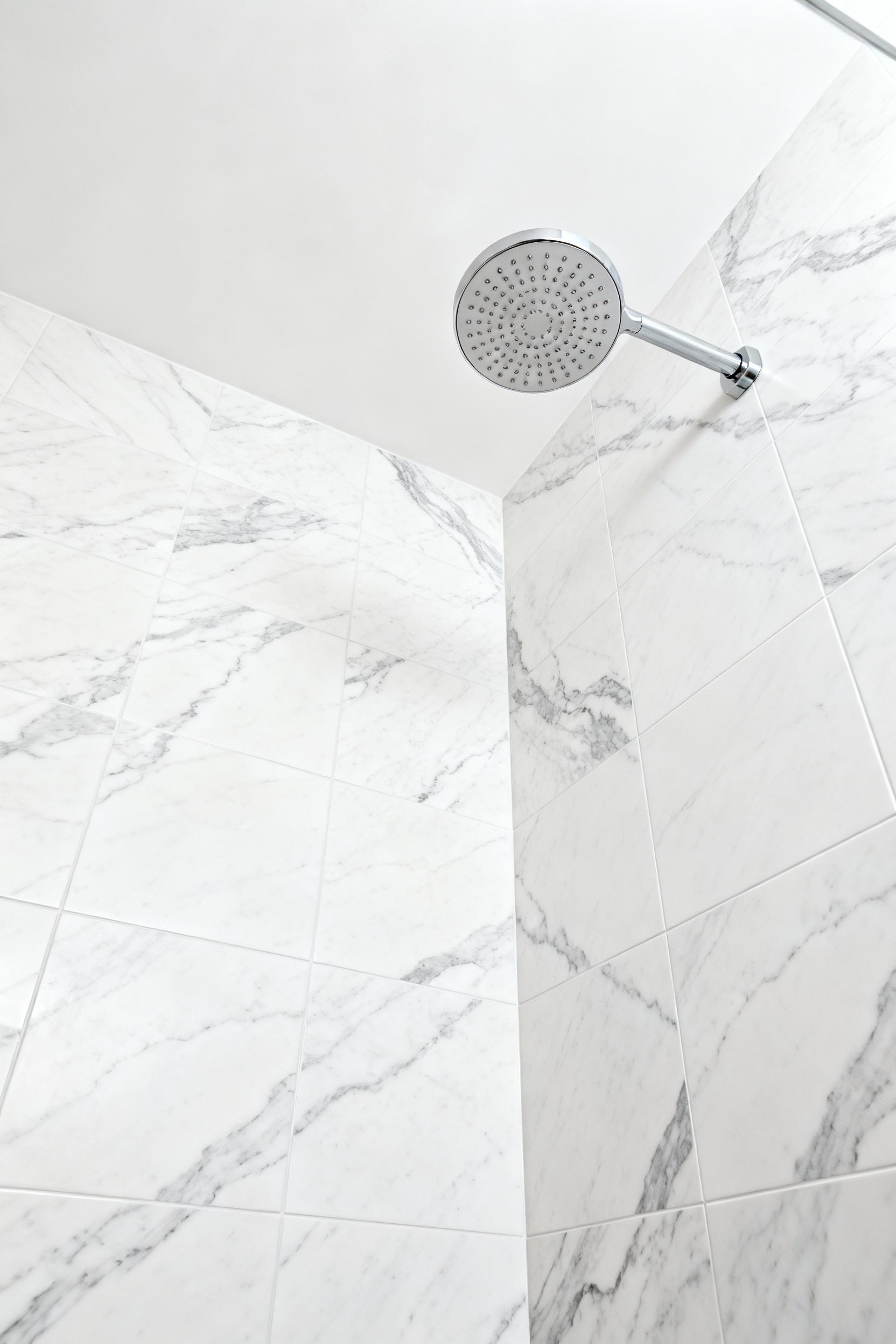 Luxury bathroom shower wall featuring large-format, book-matched porcelain stoneware tiles that replicate Statuario marble, showcasing seamless design and minimal grout lines, enhancing a modern bathscape.