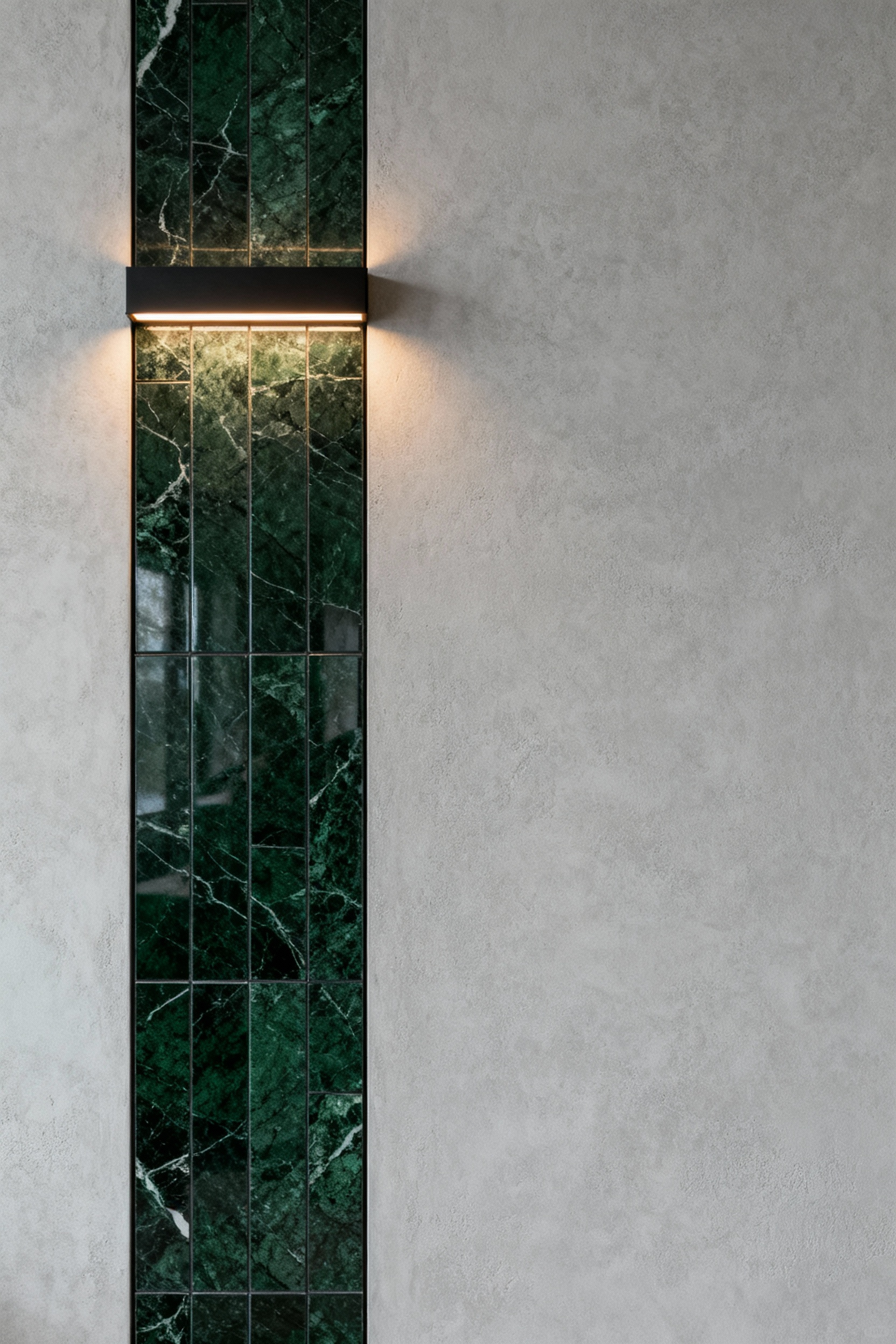 Luxury bathroom wall featuring a contrasting design with a polished dark green marble panel embedded into a matte light grey micro-cement wall, showcasing a curated disruption aesthetic. Modern architectural lighting subtly illuminates the textures and reflective differences.