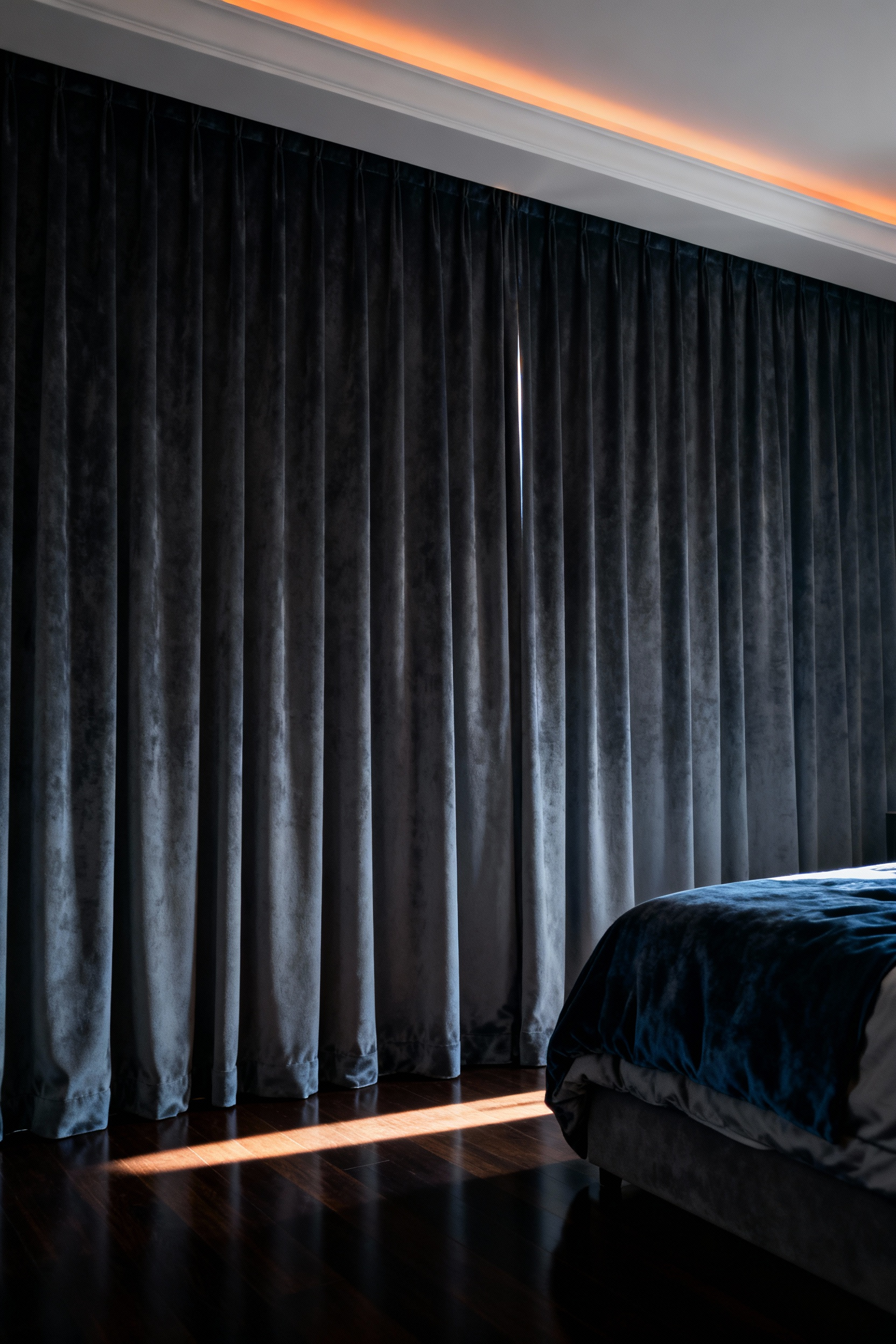 A photograph of a luxurious, dark bedroom featuring heavy, charcoal blackout drapery completely drawn, emphasizing sophisticated sleep hygiene and near-absolute darkness.