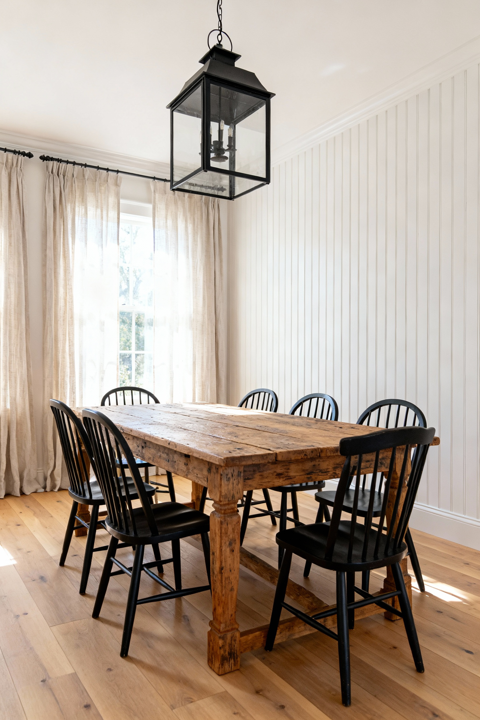 Farmhouse dining room featuring crisp white vertical board-and-batten paneling, a rustic reclaimed wood dining table, and black Windsor chairs, illustrating how vertical lines increase perceived room height.