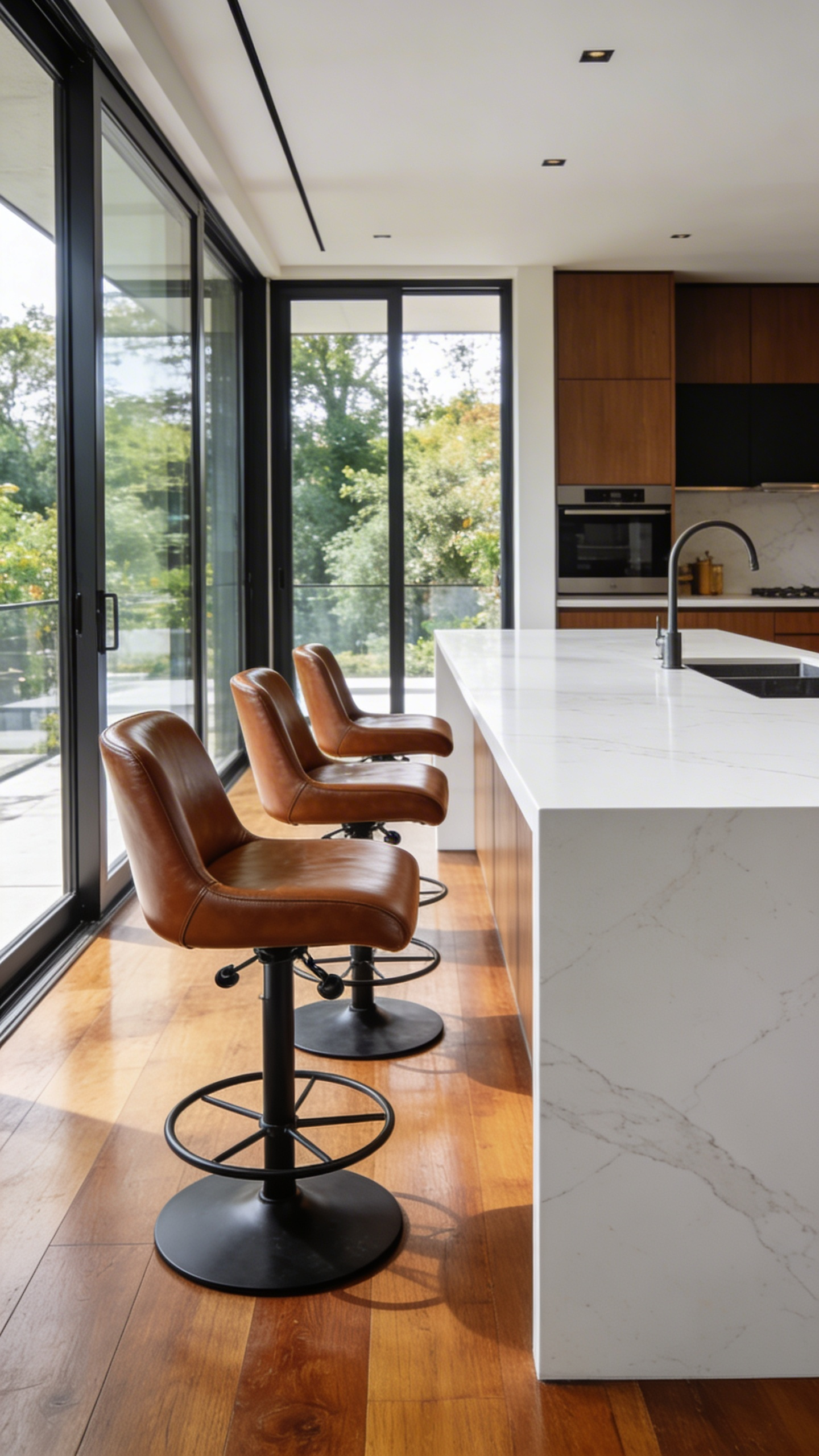 A spacious modern kitchen featuring a white quartz island and three brown leather swivel stools turned at varying angles.