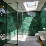 A luxurious bathroom featuring emerald green Zellige wall tiles that catch and scatter natural sunlight to create a shimmering effect.