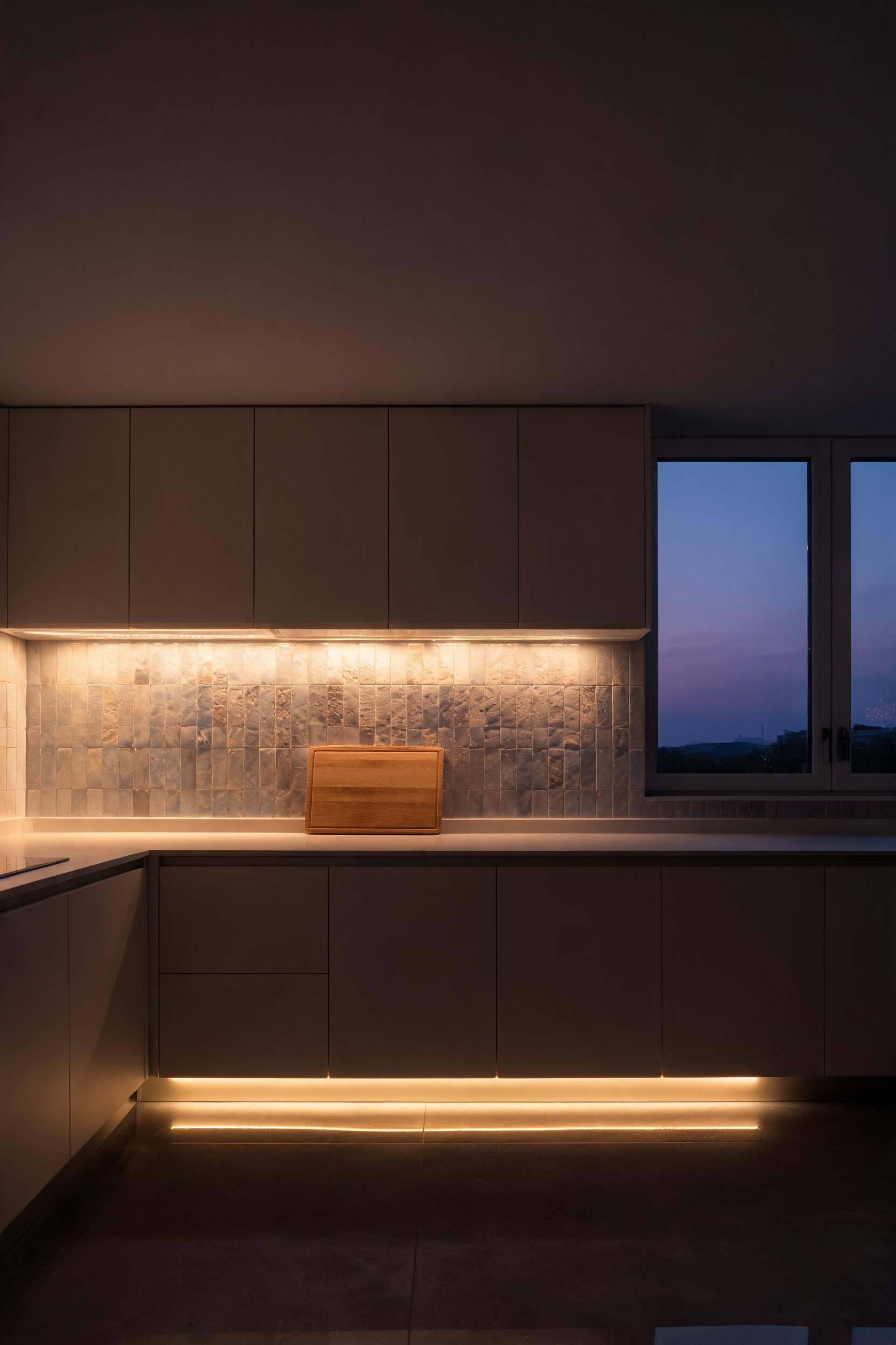 Under-cabinet LED strips task-light the counter at 2700K while toe-kick strips create a floating effect at floor level -- two light layers that replace an entire ceiling fixture arrangement.